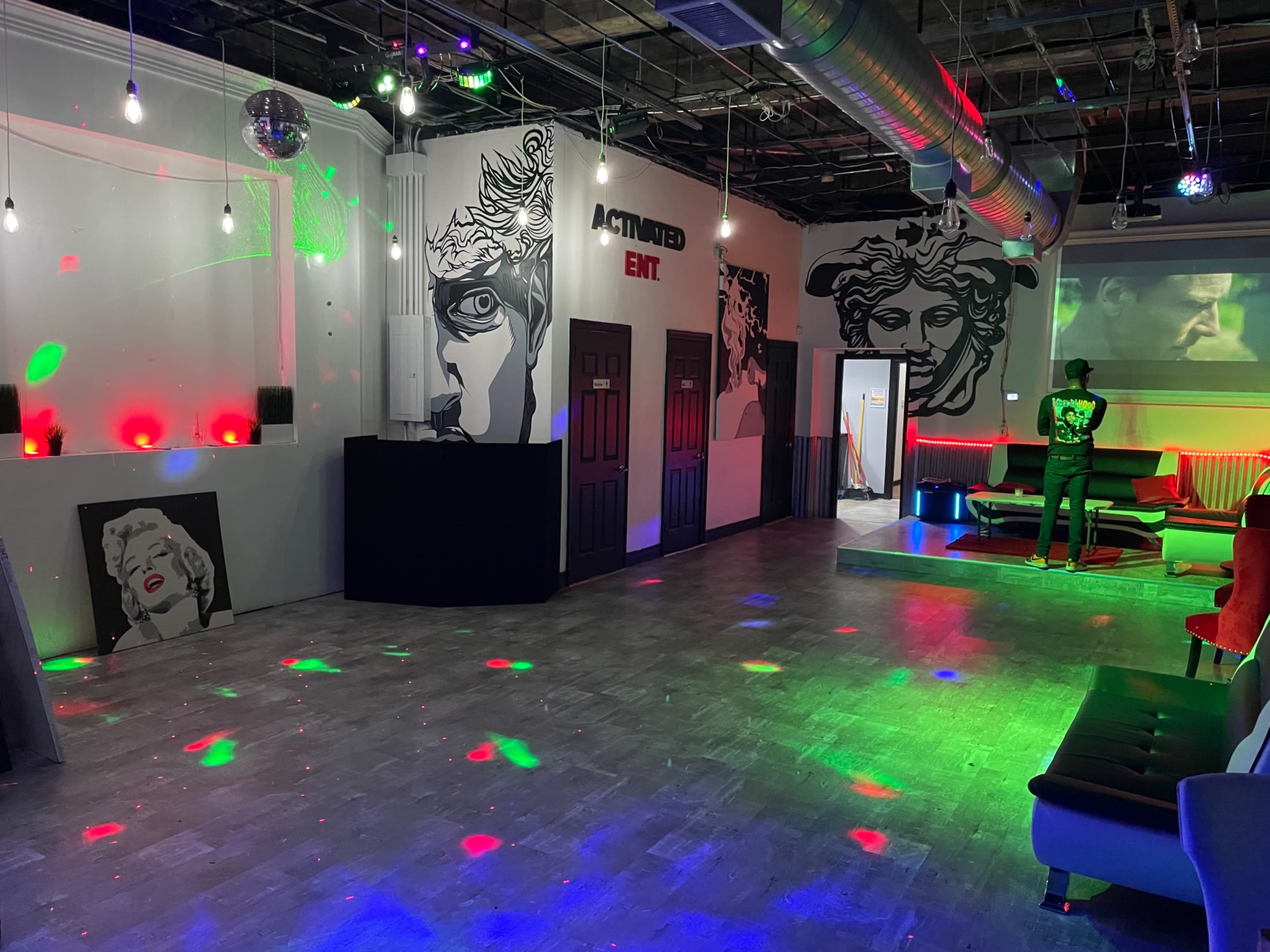 An empty entertainment space featuring colorful lights, two large wall murals, and a central area with seating.