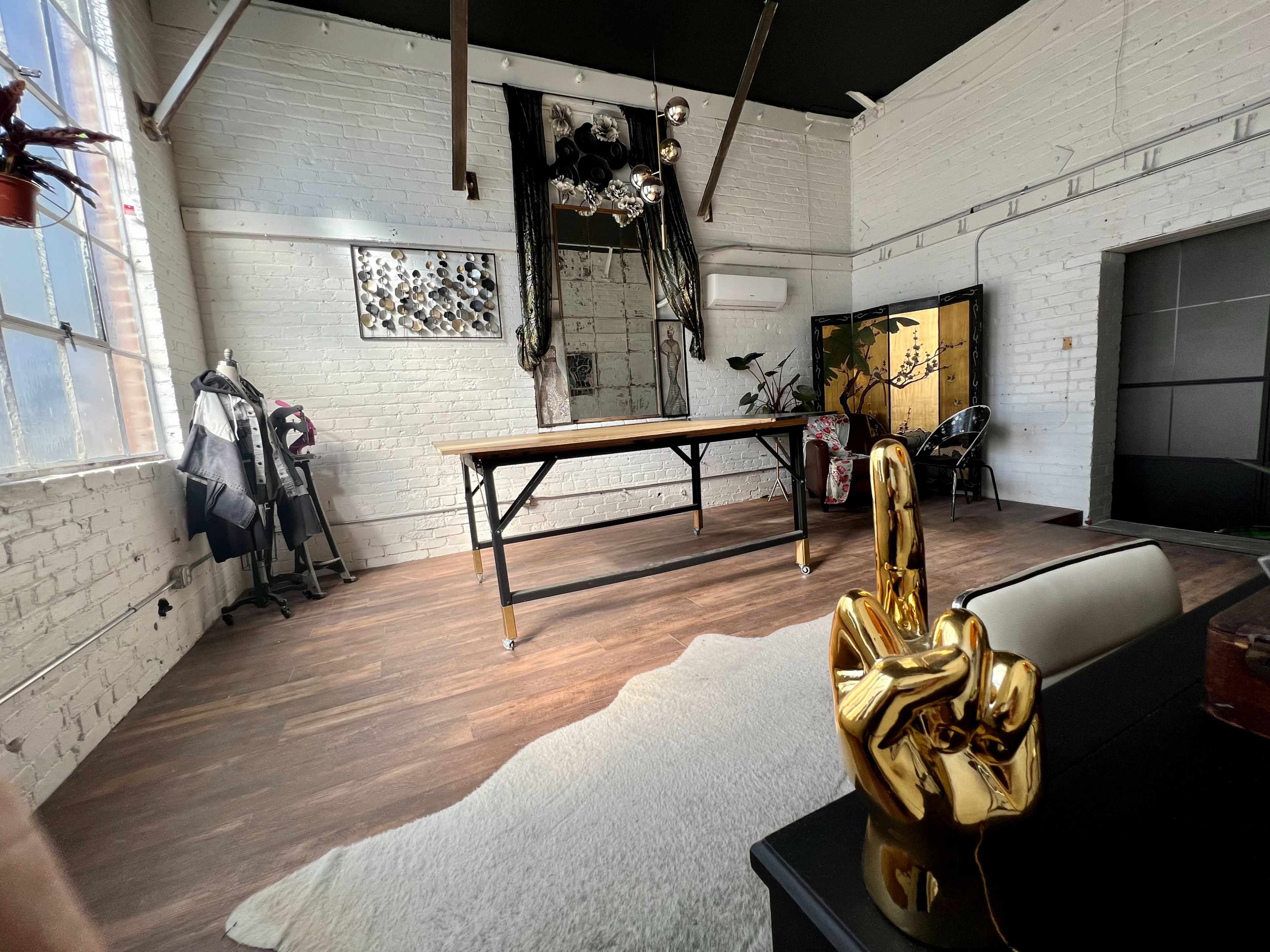 A spacious, brightly lit interior featuring a large wooden table, decorative sculptures, and a mix of furniture against a backdrop of white brick walls.