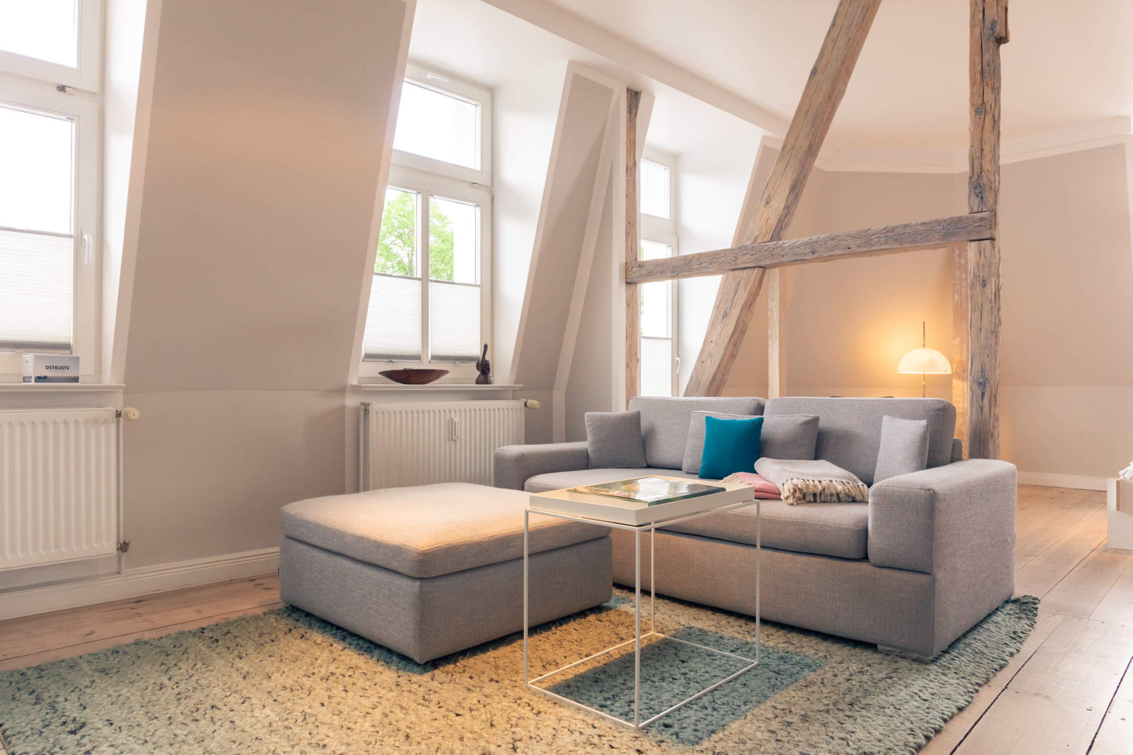 A modern living room with a gray sofa and matching ottoman, a glass coffee table, and large windows that provide natural light.