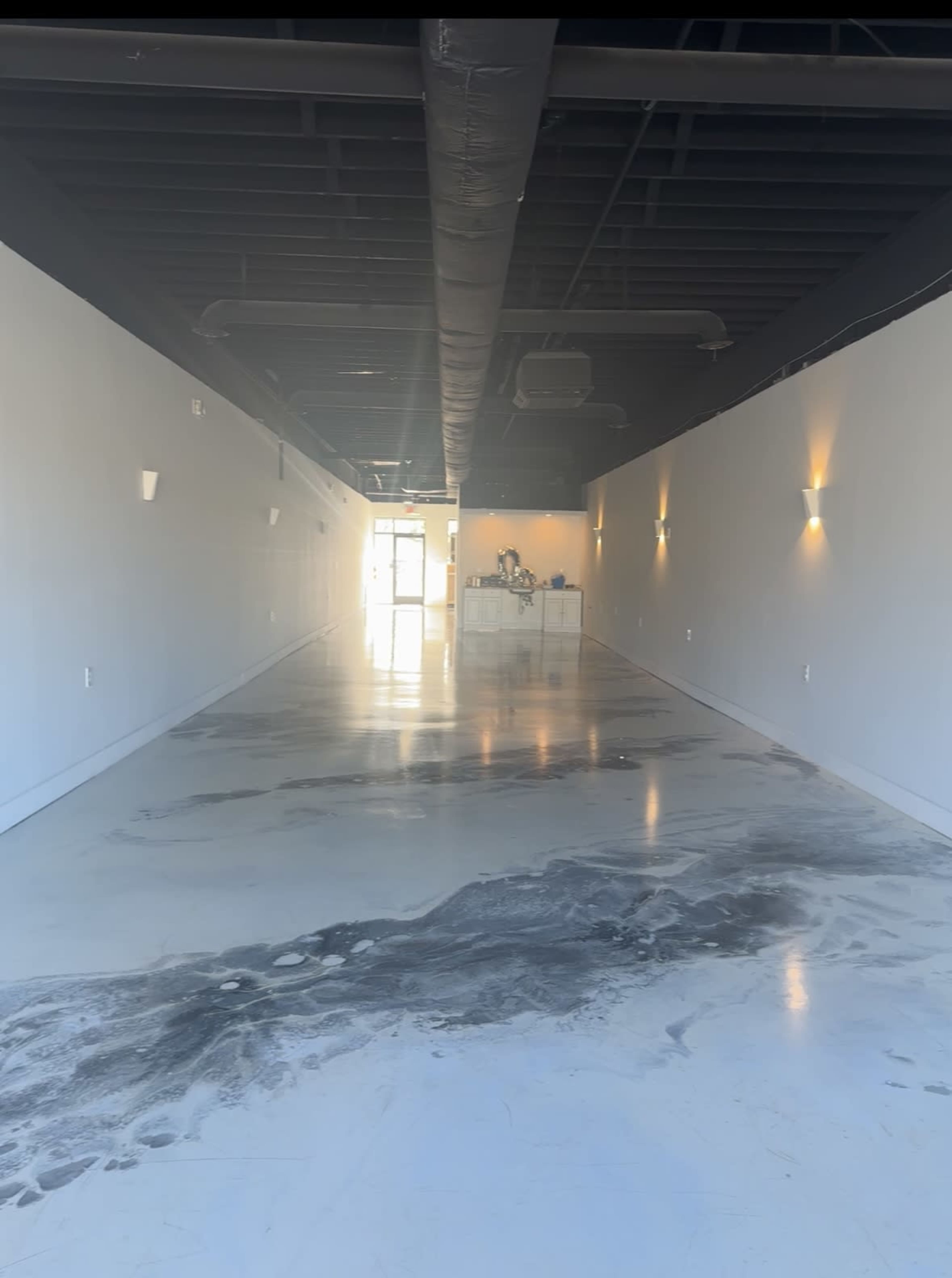 An empty commercial space with polished concrete floors and simple wall lighting.