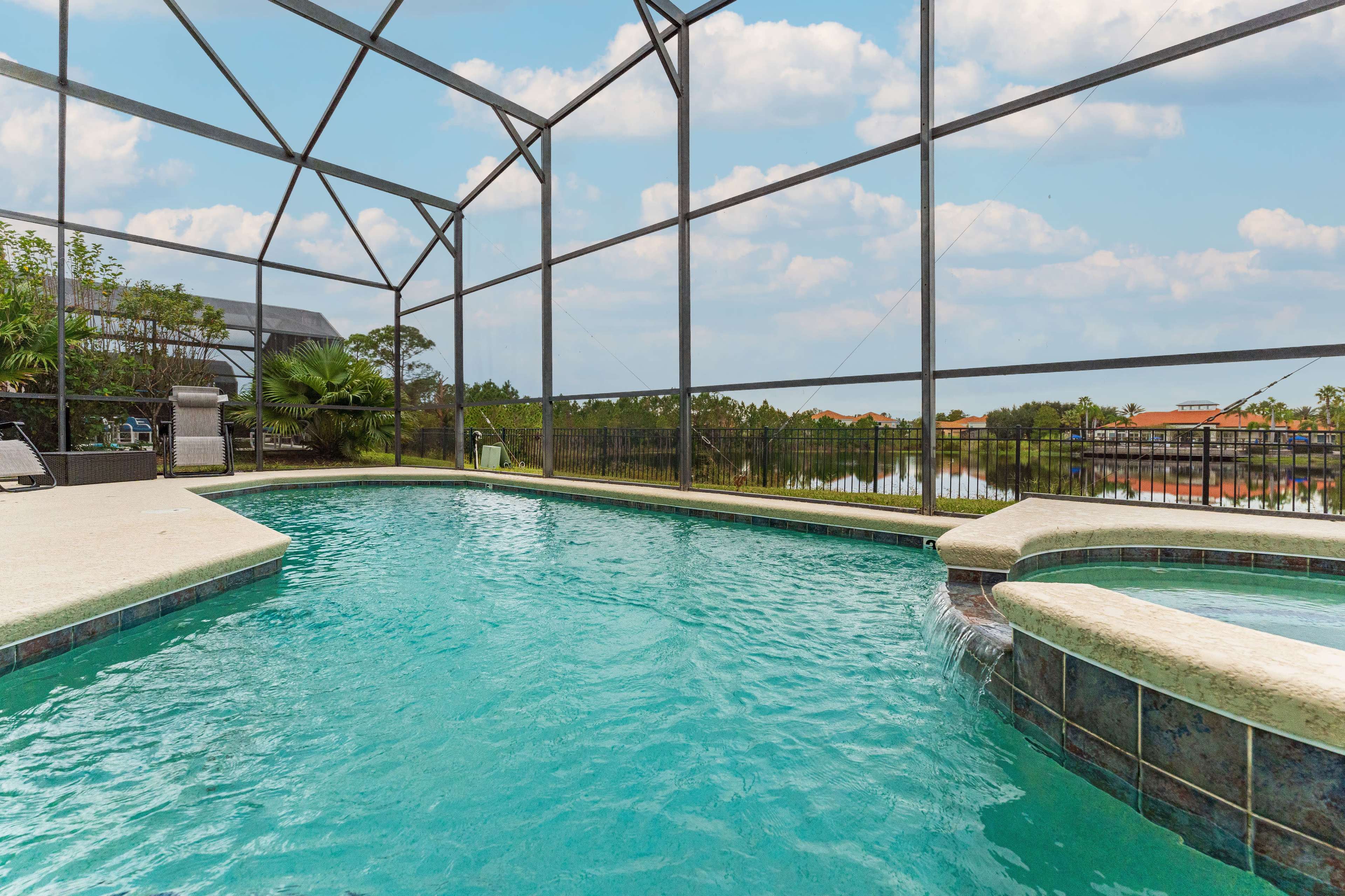A swimming pool surrounded by a screen enclosure, featuring a spa and views of nearby homes and greenery.