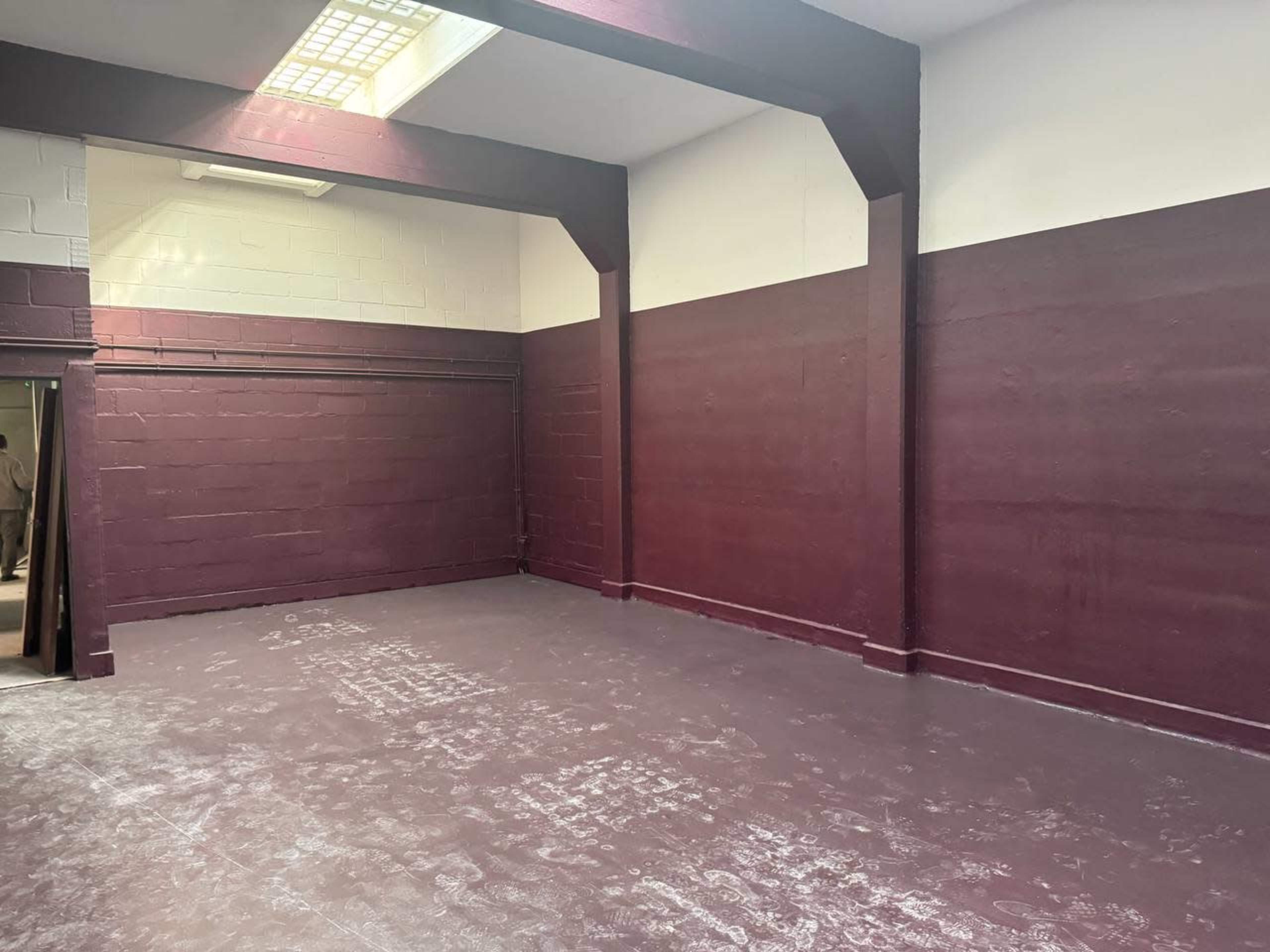 The image shows a large, empty room with maroon-painted walls and a plain concrete floor.
