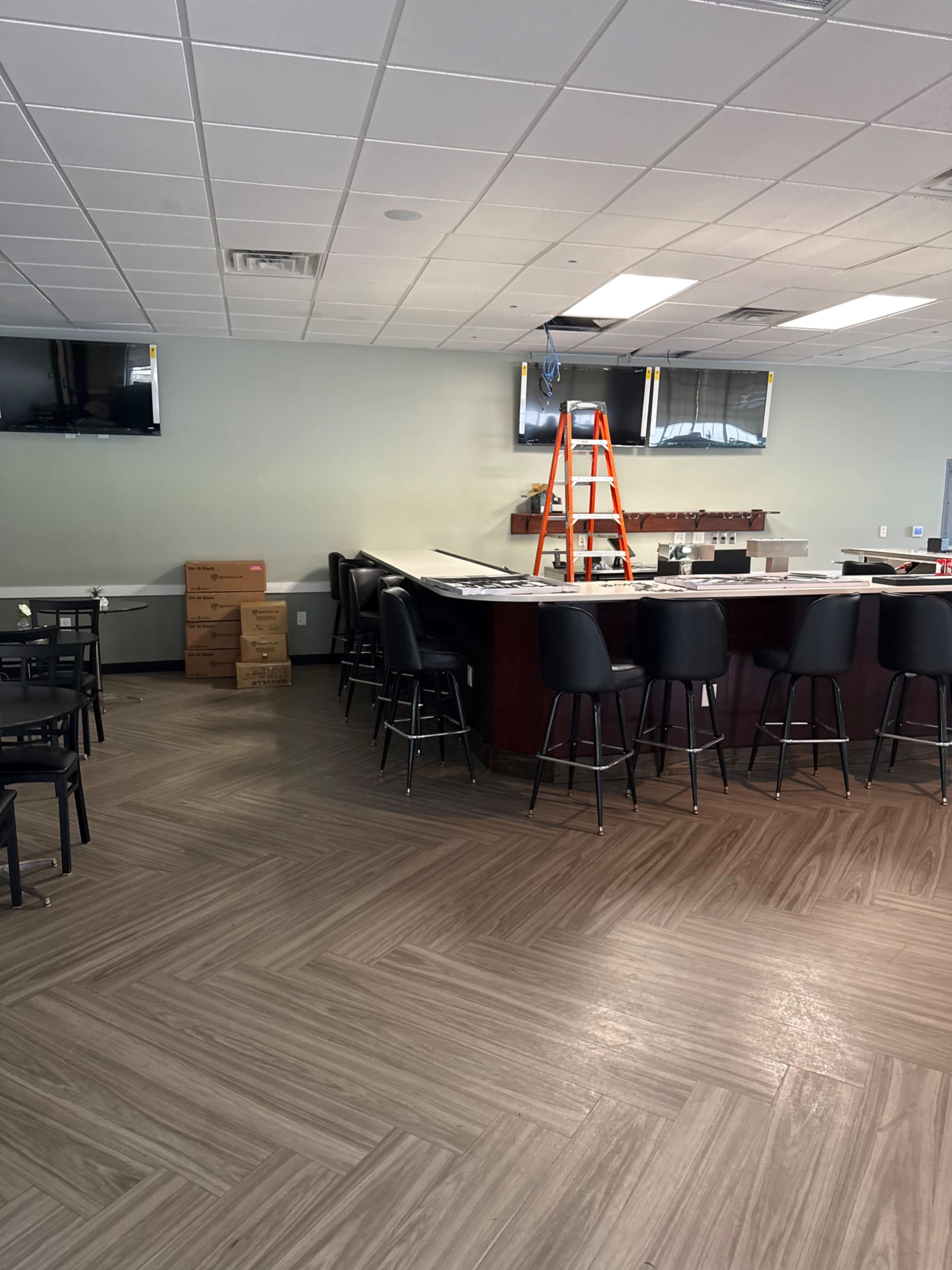 The image shows a partially furnished restaurant interior with a bar area, seating, a ladder, and several boxes stacked in the corner.