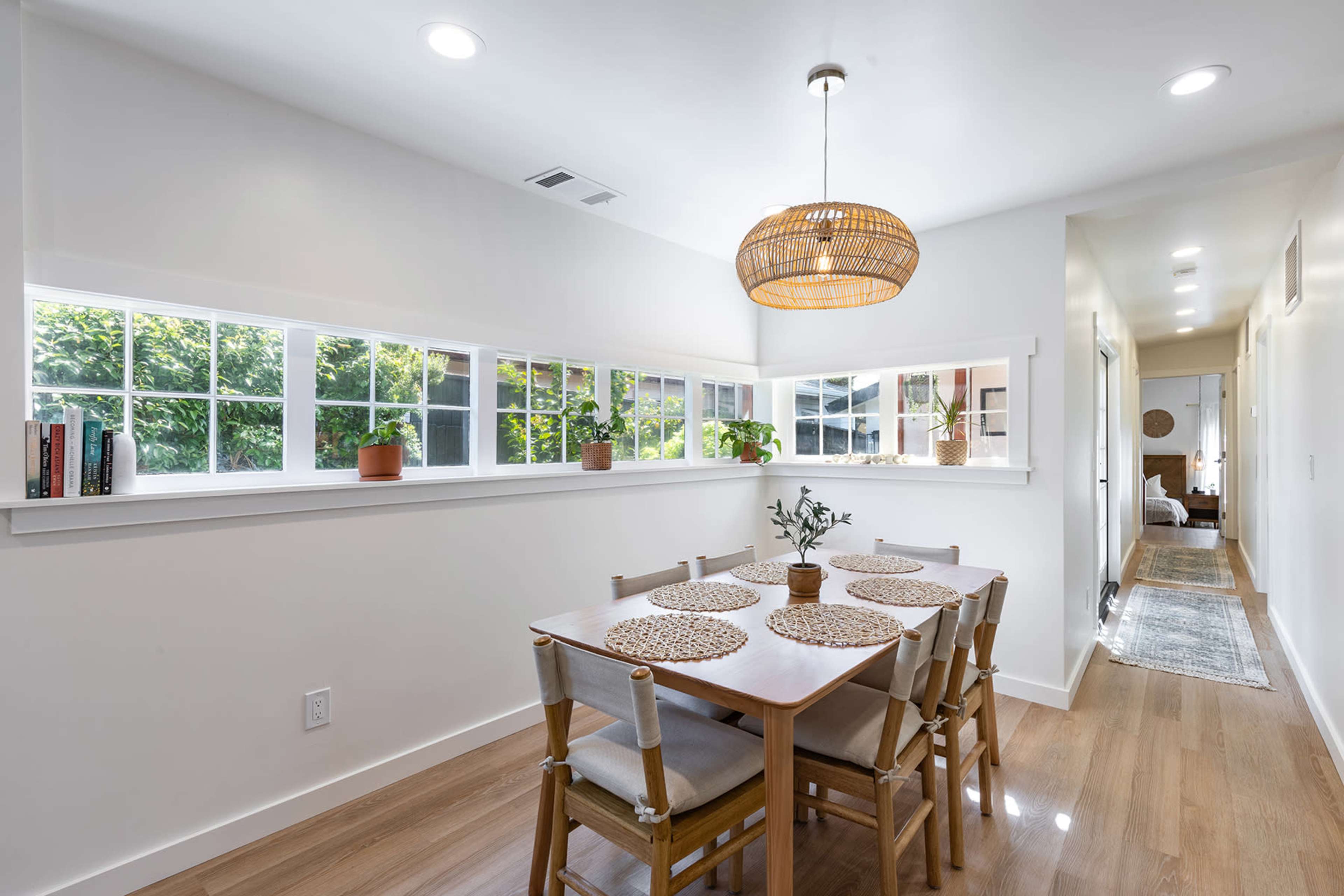 A modern dining area with a wooden table, six chairs, and a large window, surrounded by potted plants.