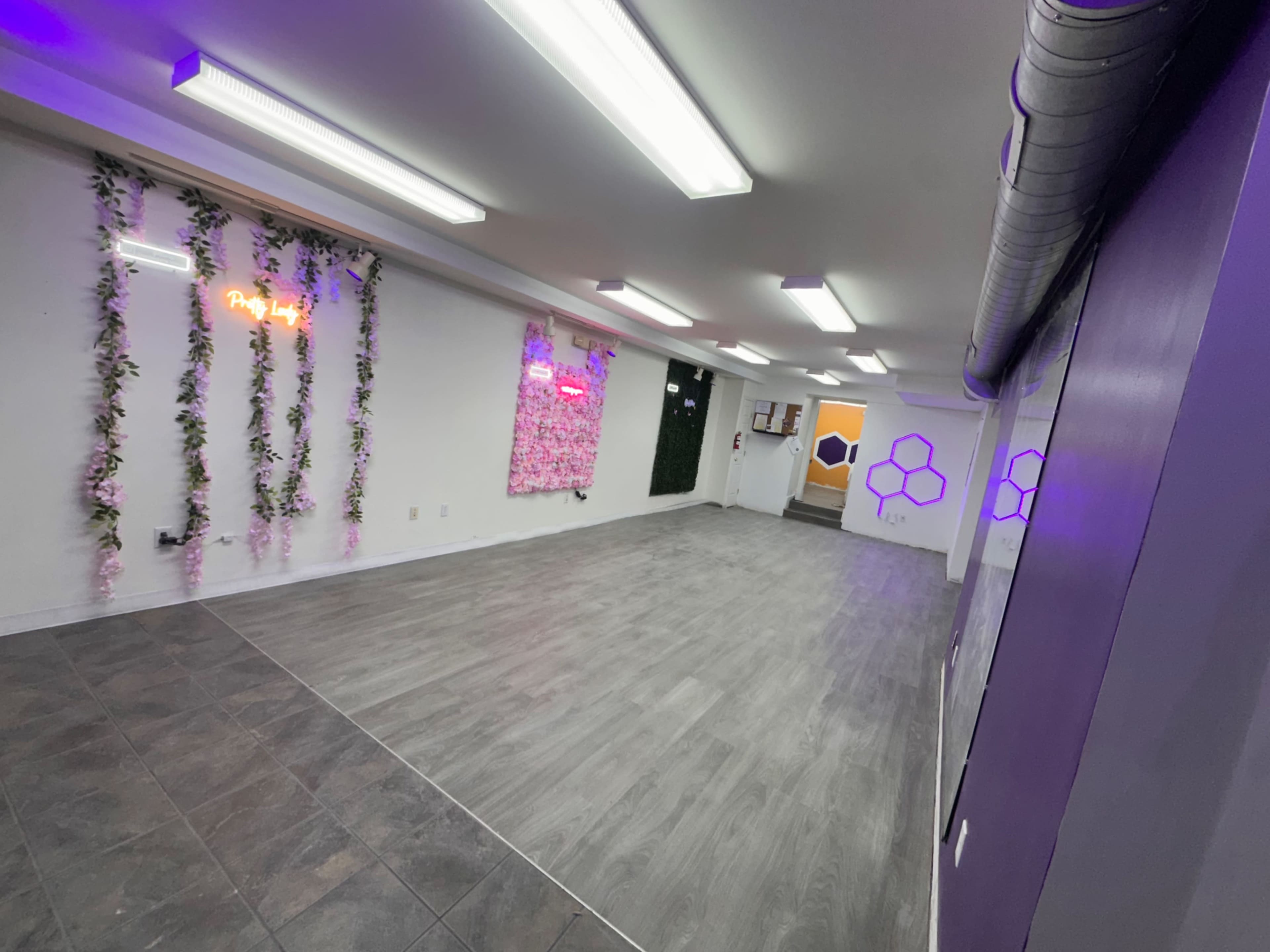 The image shows a spacious, well-lit room with gray flooring, decorated with floral elements and neon signs on the walls.