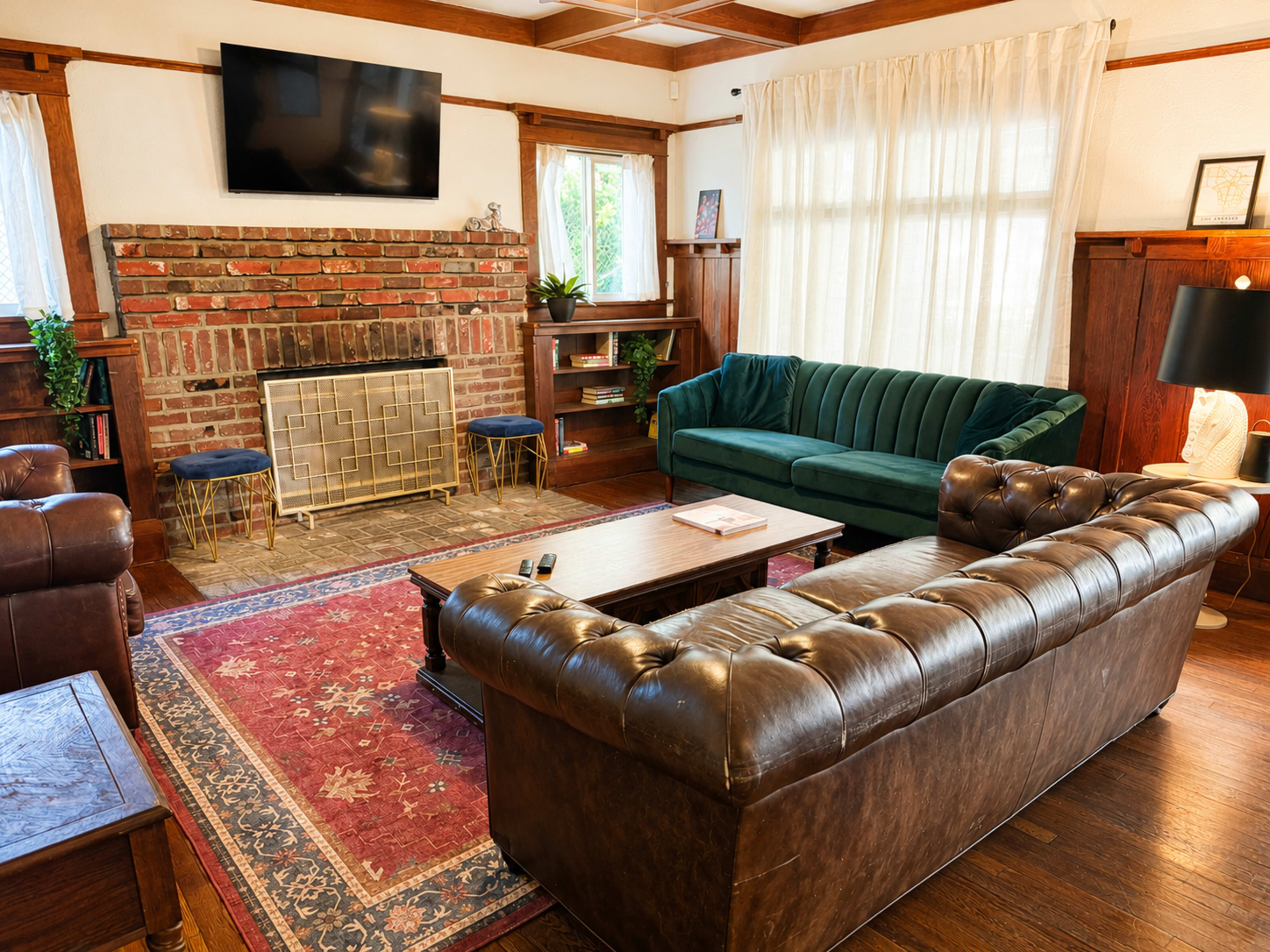 The living room features a brick fireplace, a green velvet sofa, a brown leather chesterfield couch, and wooden furniture, all arranged around a central coffee table and rug.