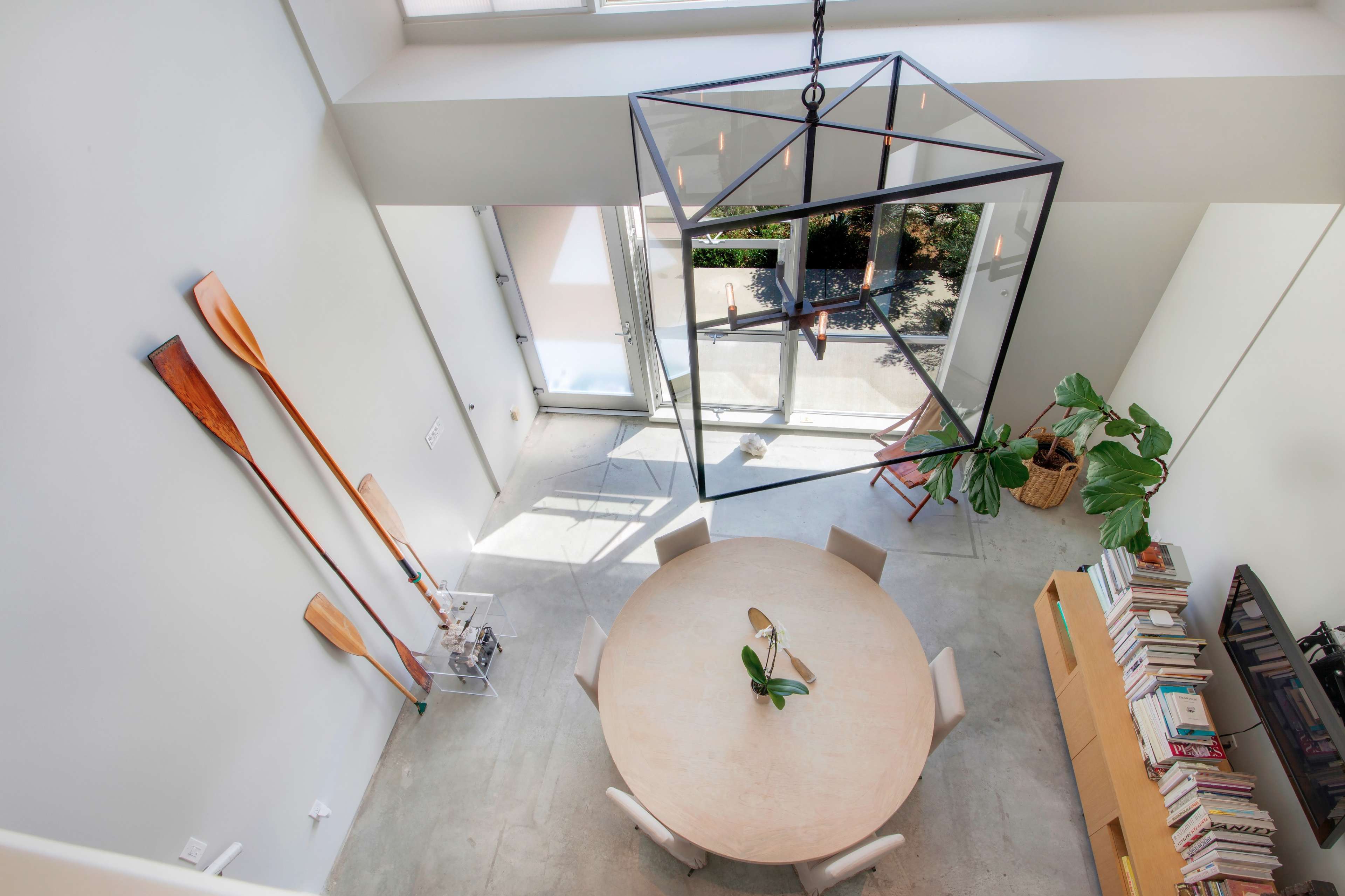 The image shows a spacious, modern indoor area featuring a round table, a large geometric light fixture, and decorative elements like oars and bookshelves.