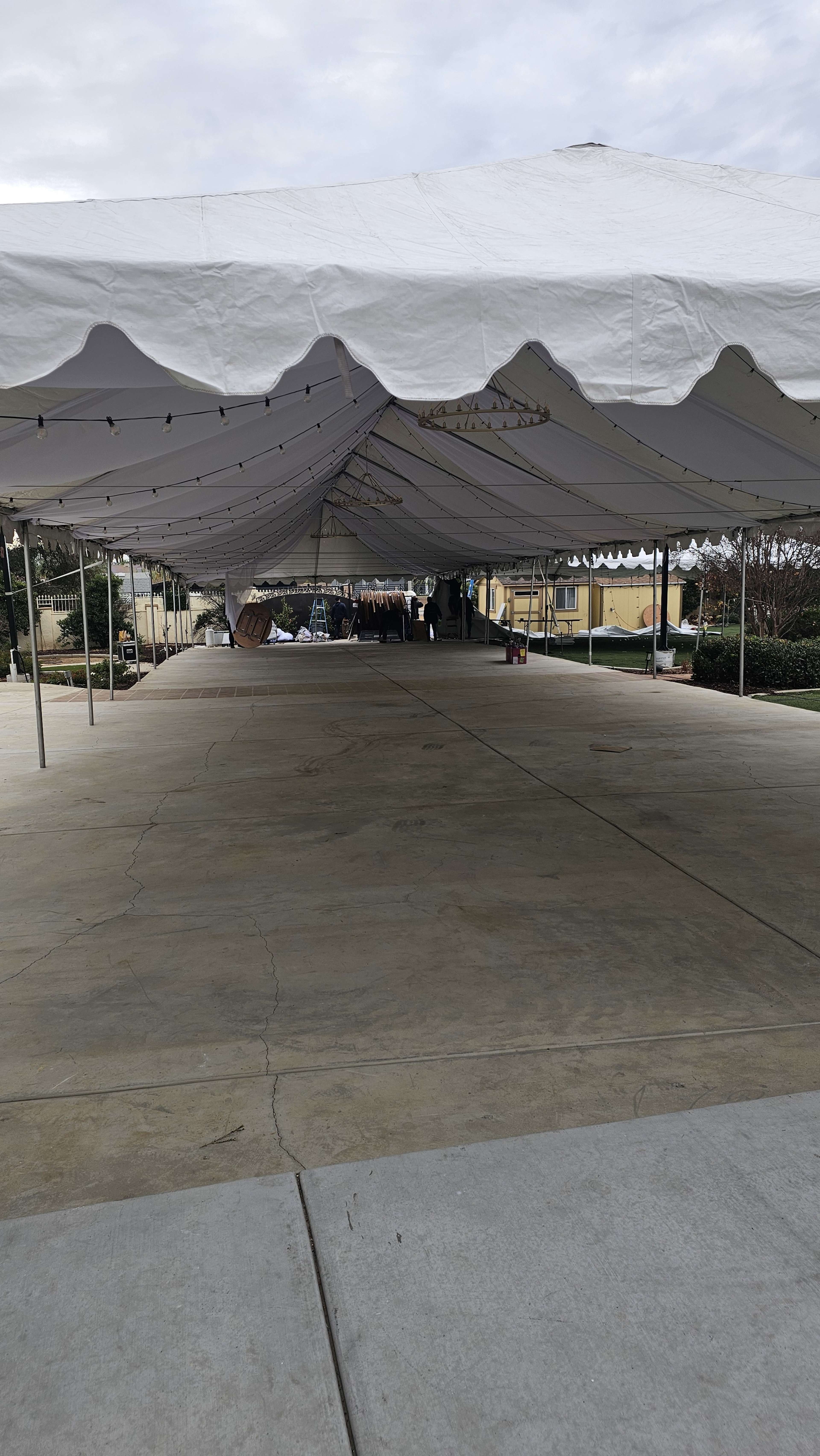 A large white tent is set up on a concrete surface, with visible support poles and overhead lights.