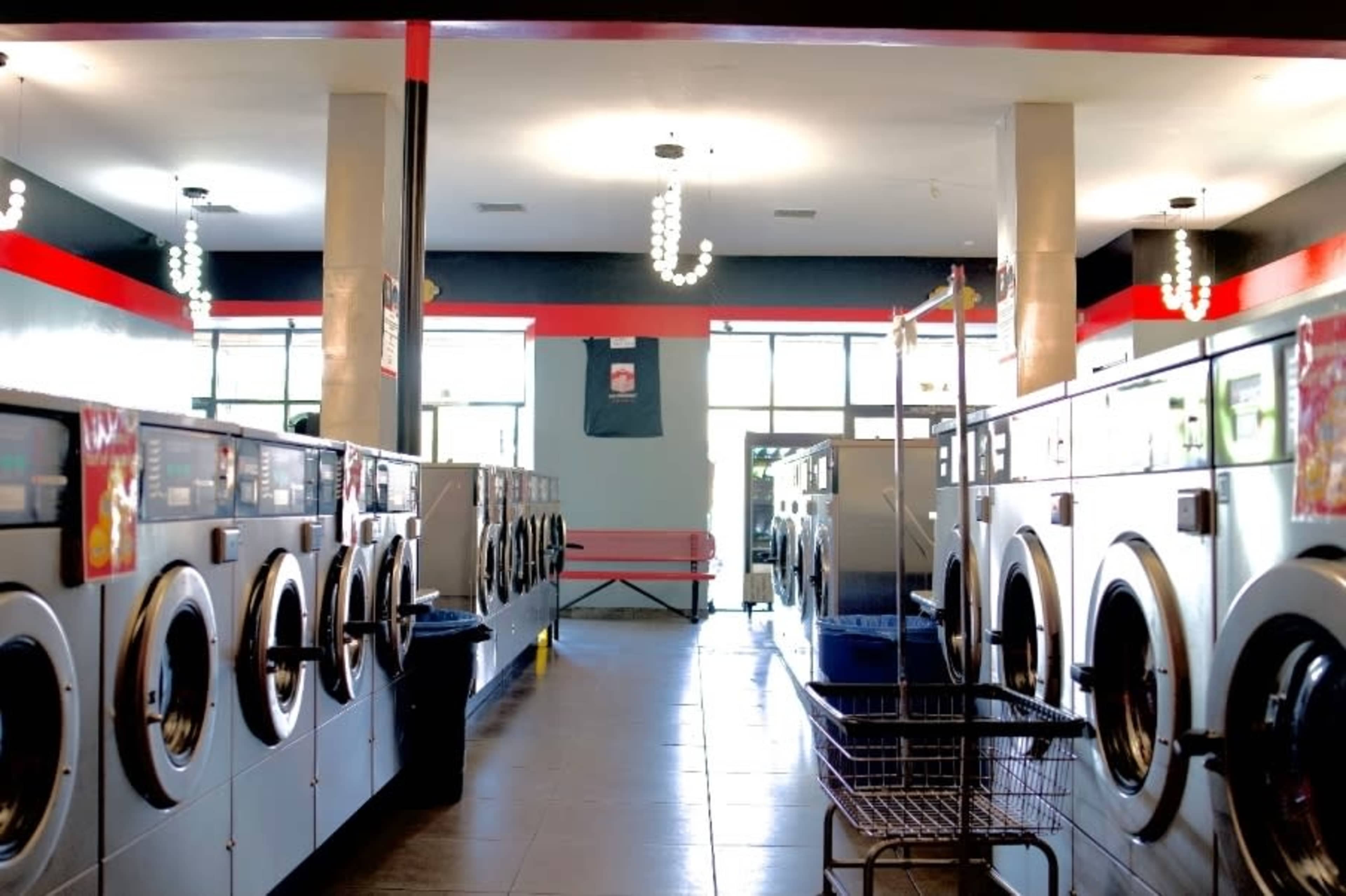 The image shows an indoor laundromat with rows of washing machines and a public seating area in the background.