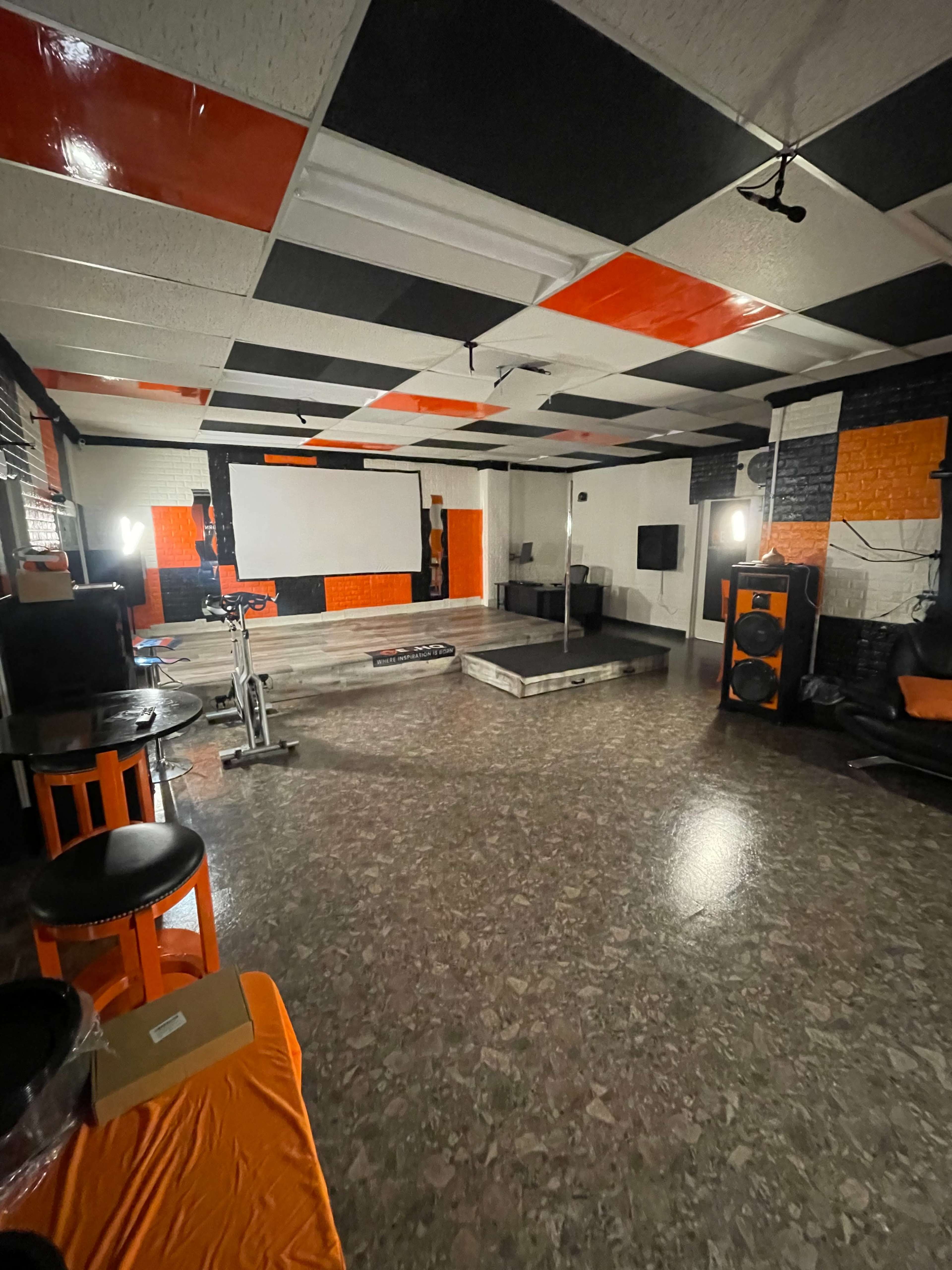 A spacious, empty room with a large projection screen on one wall, black and orange decor, and several pieces of furniture arranged around the space.