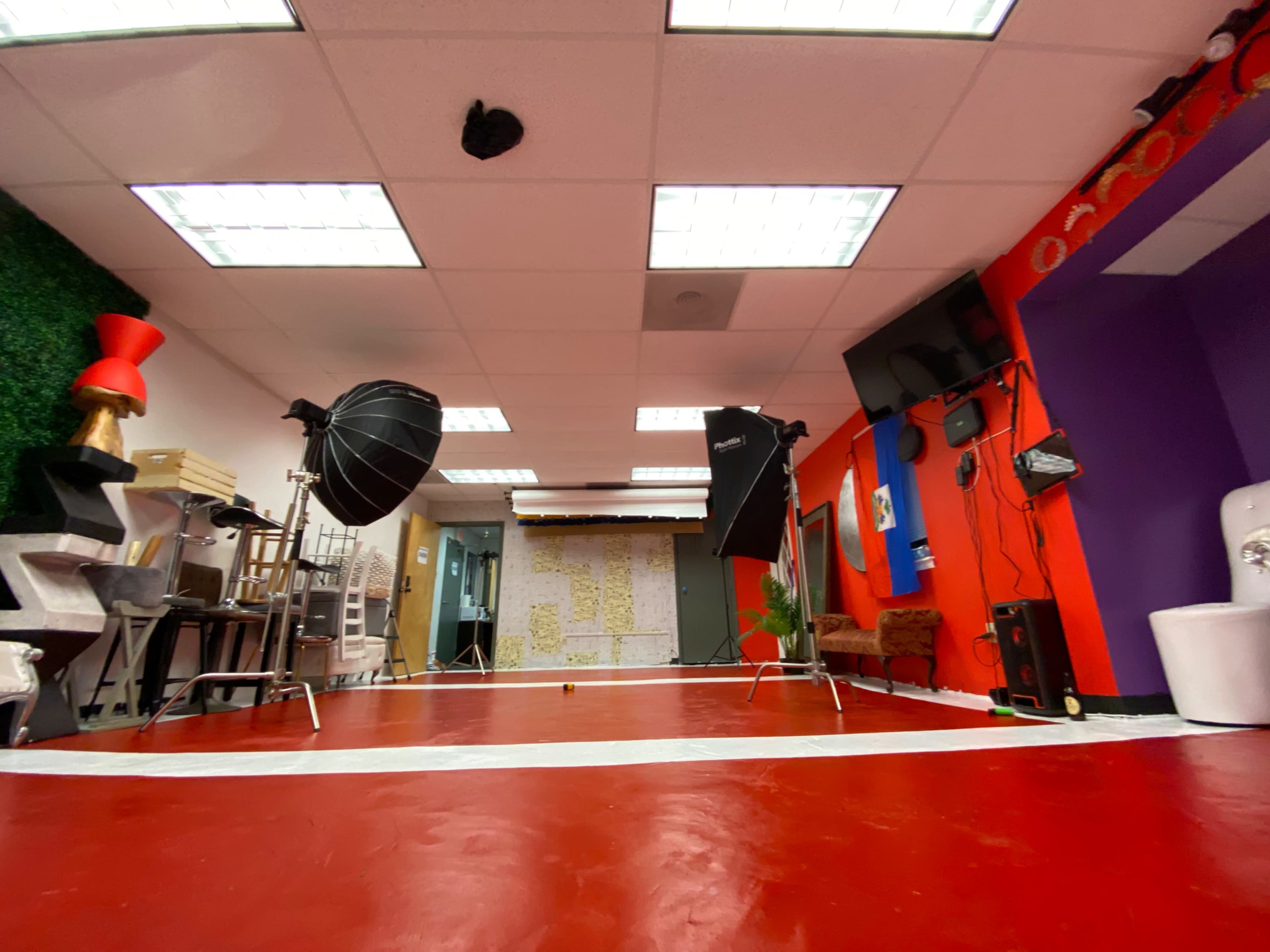 A spacious studio with a red floor, two large photography lights, and colorful walls adorned with various decorations.