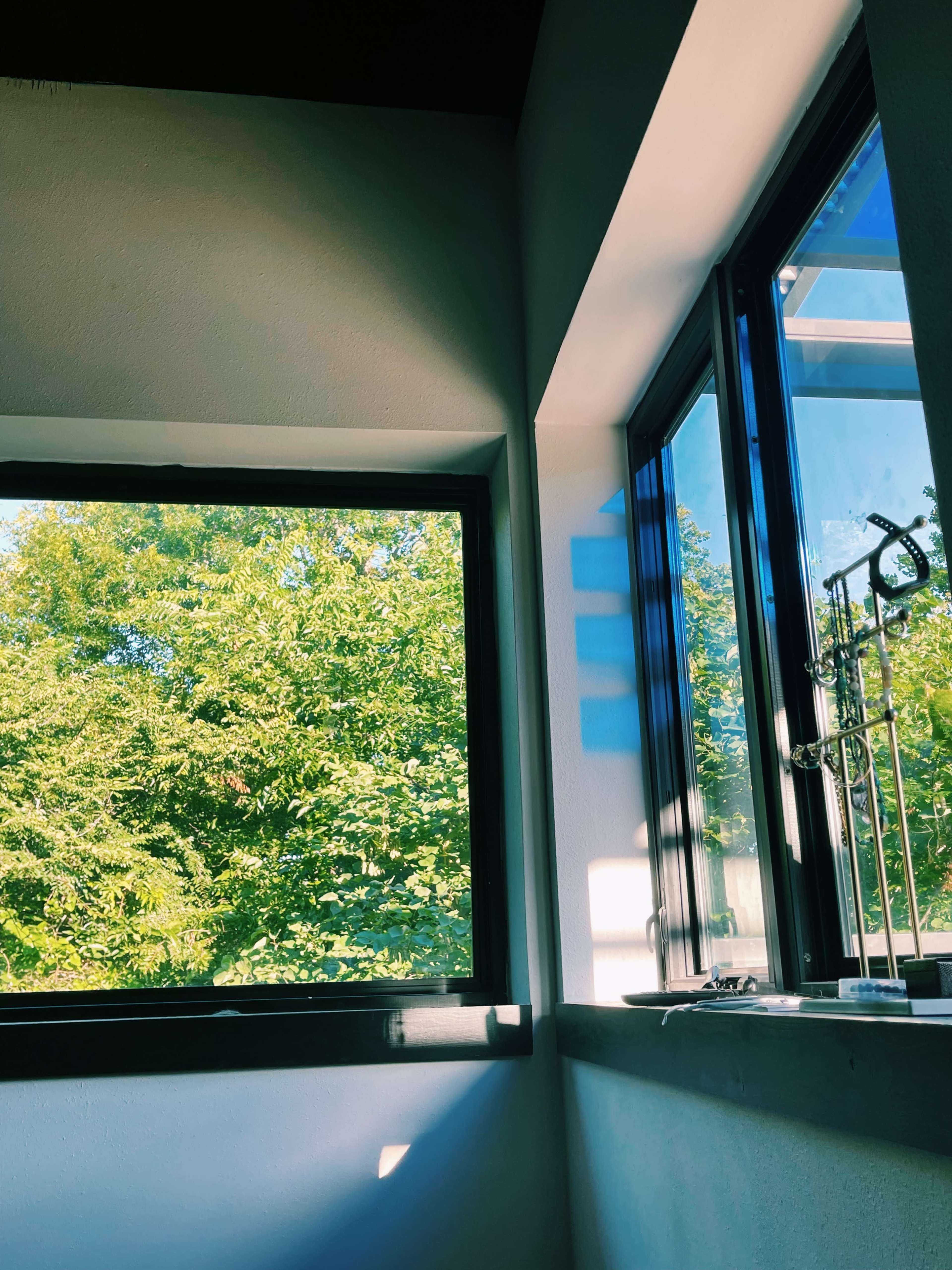 A corner of a room with large windows framing a view of lush green trees outside.