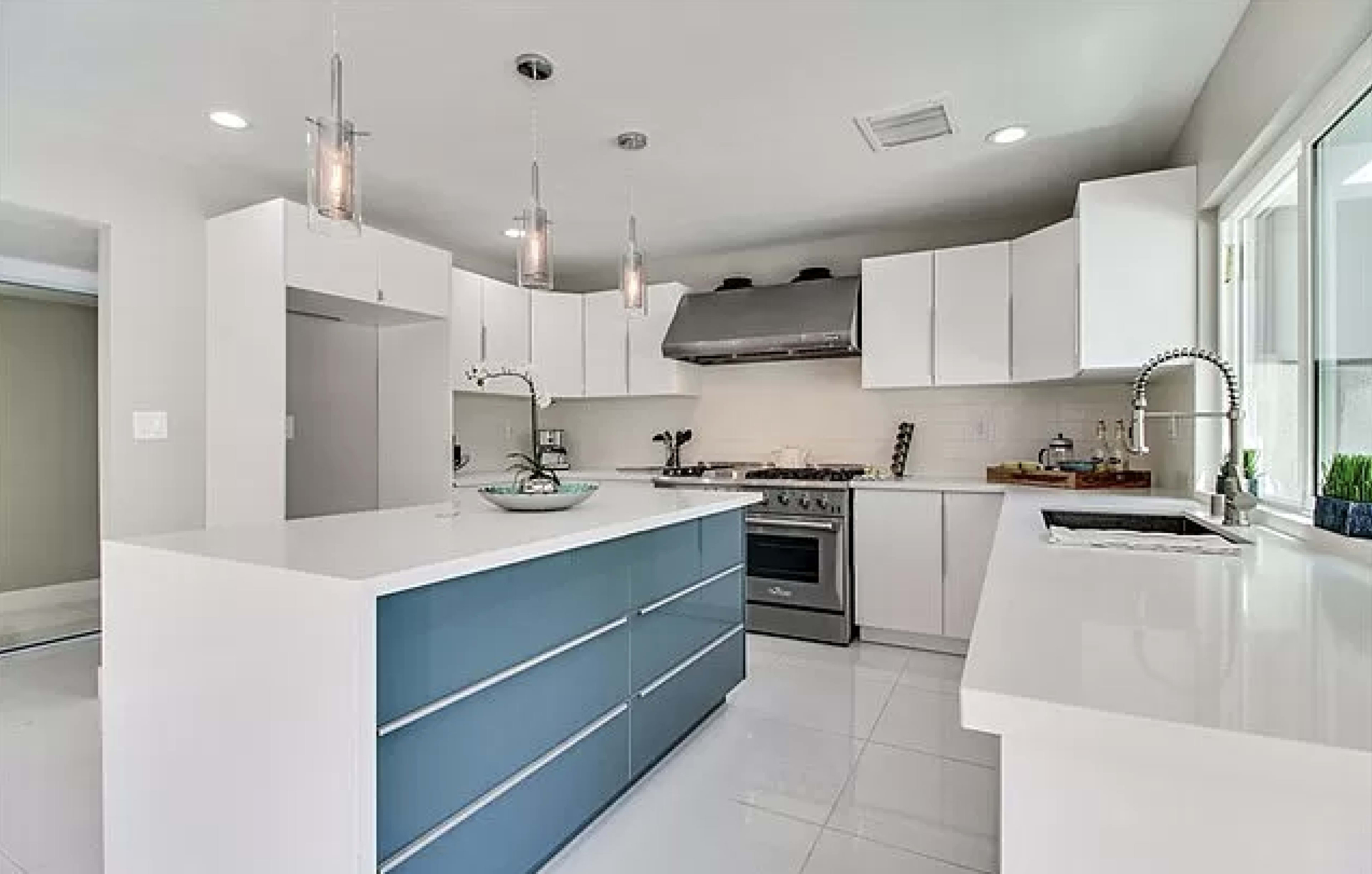 A modern kitchen featuring white cabinetry, a blue island with drawers, stainless steel appliances, and bright overhead lighting.