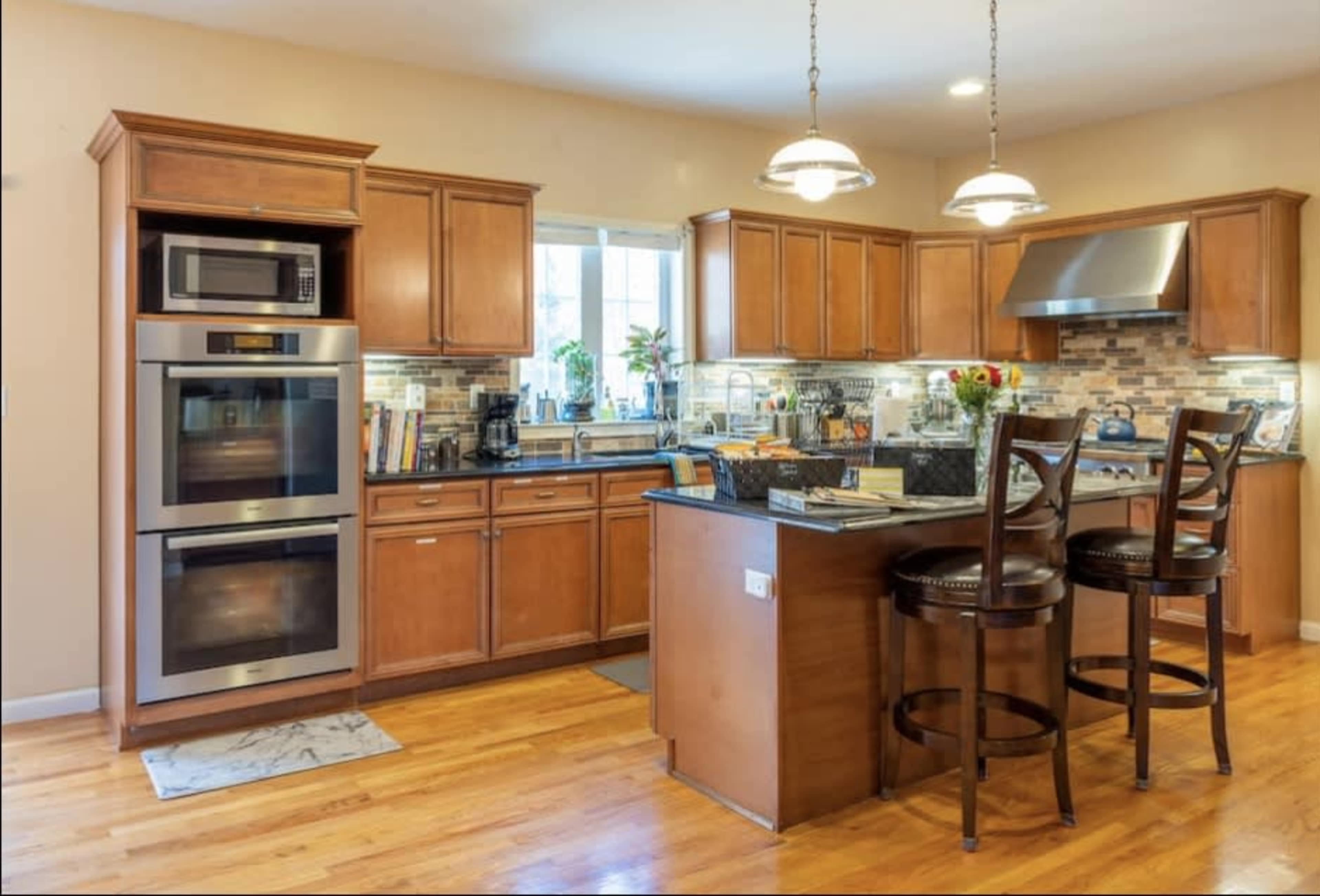 A modern kitchen with wooden cabinets, stainless steel appliances, and a central island with two bar stools.
