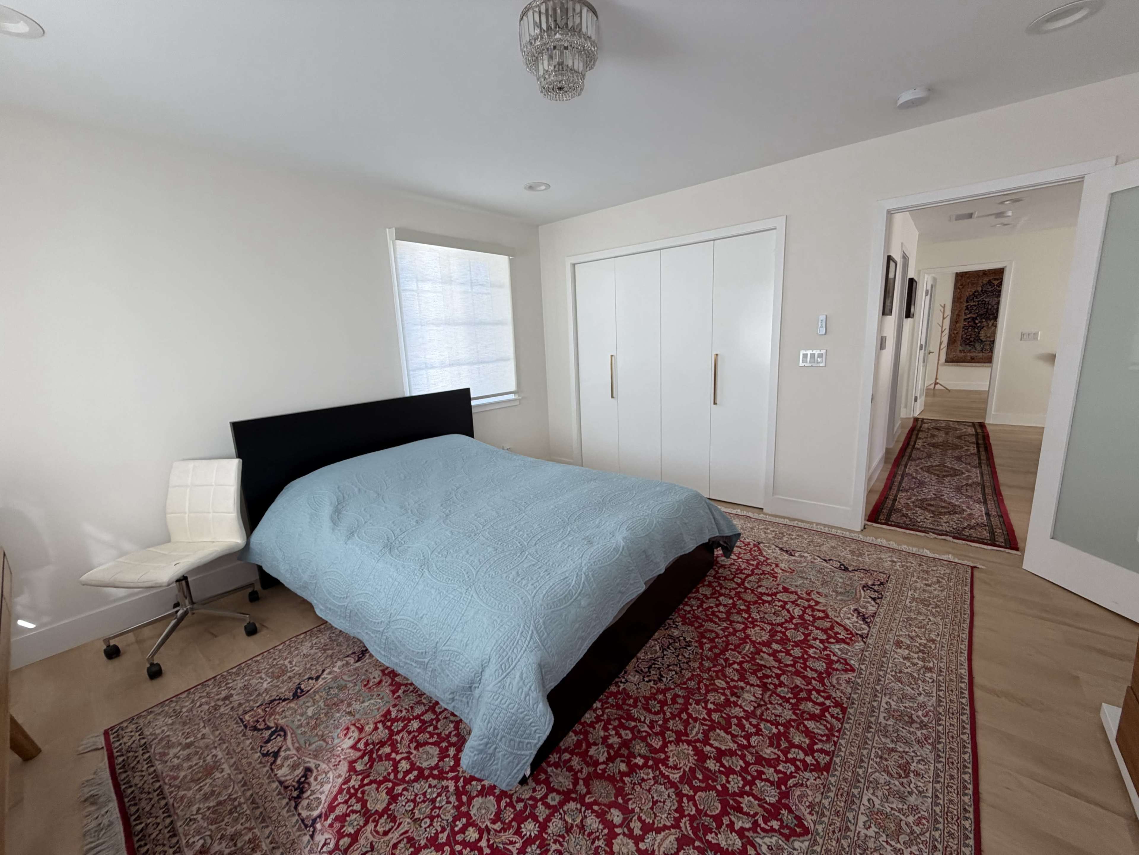 A well-lit bedroom features a bed with a light blue coverlet, a patterned area rug, and a sliding door closet.