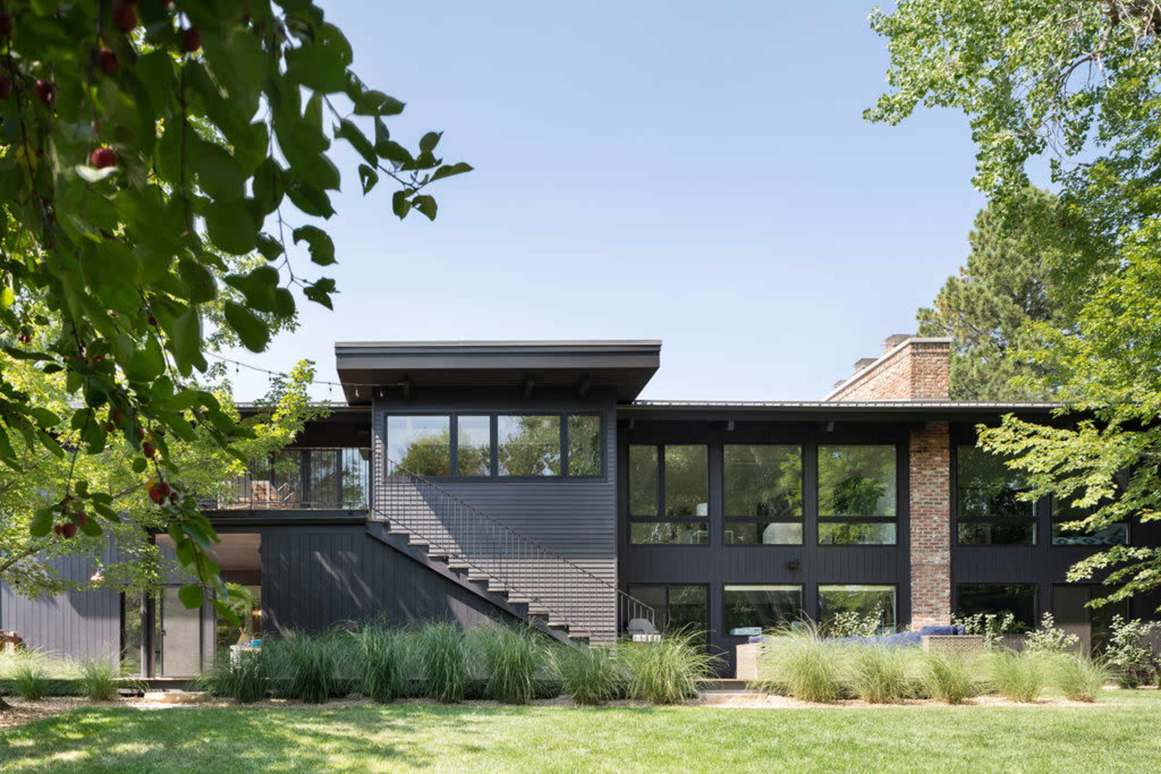 A modern two-story house features large windows and a sleek design, surrounded by greenery and grass.