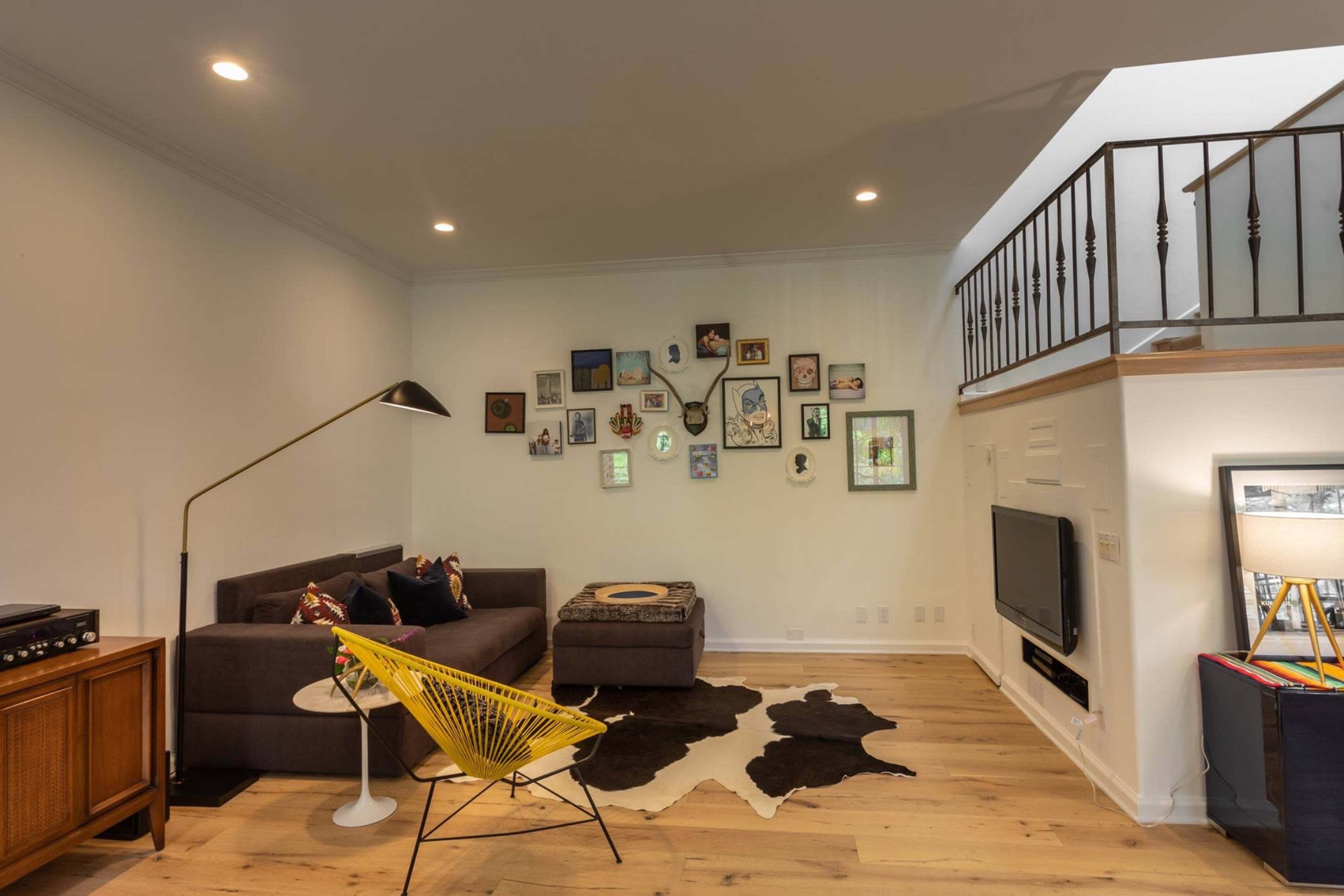 The image shows a modern living room with a sectional sofa, a coffee table on a cowhide rug, and a wall adorned with various framed pictures.