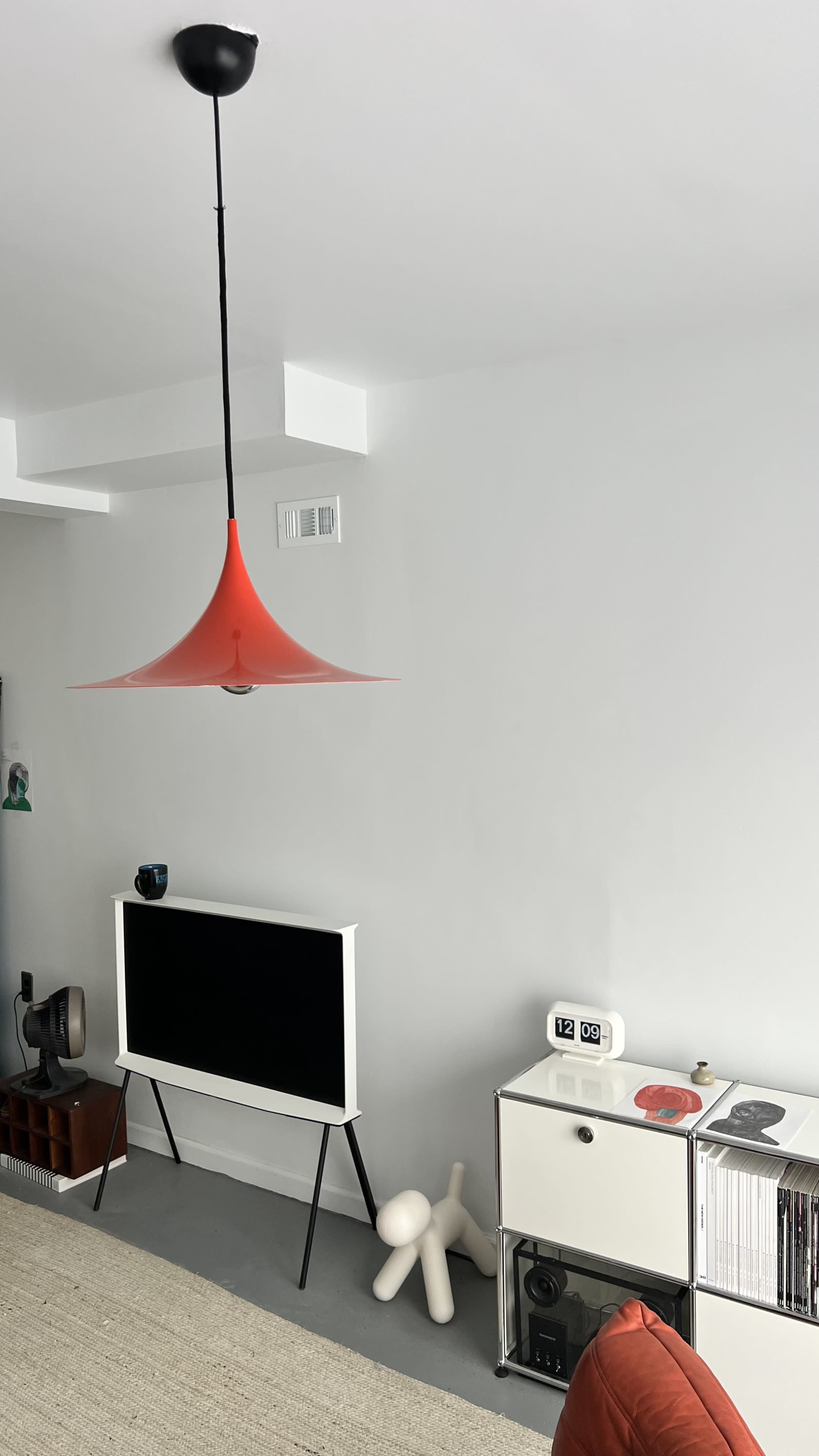 The scene features a modern living room with a red pendant lamp, a white television stand, and a decorative sculpture on the floor.
