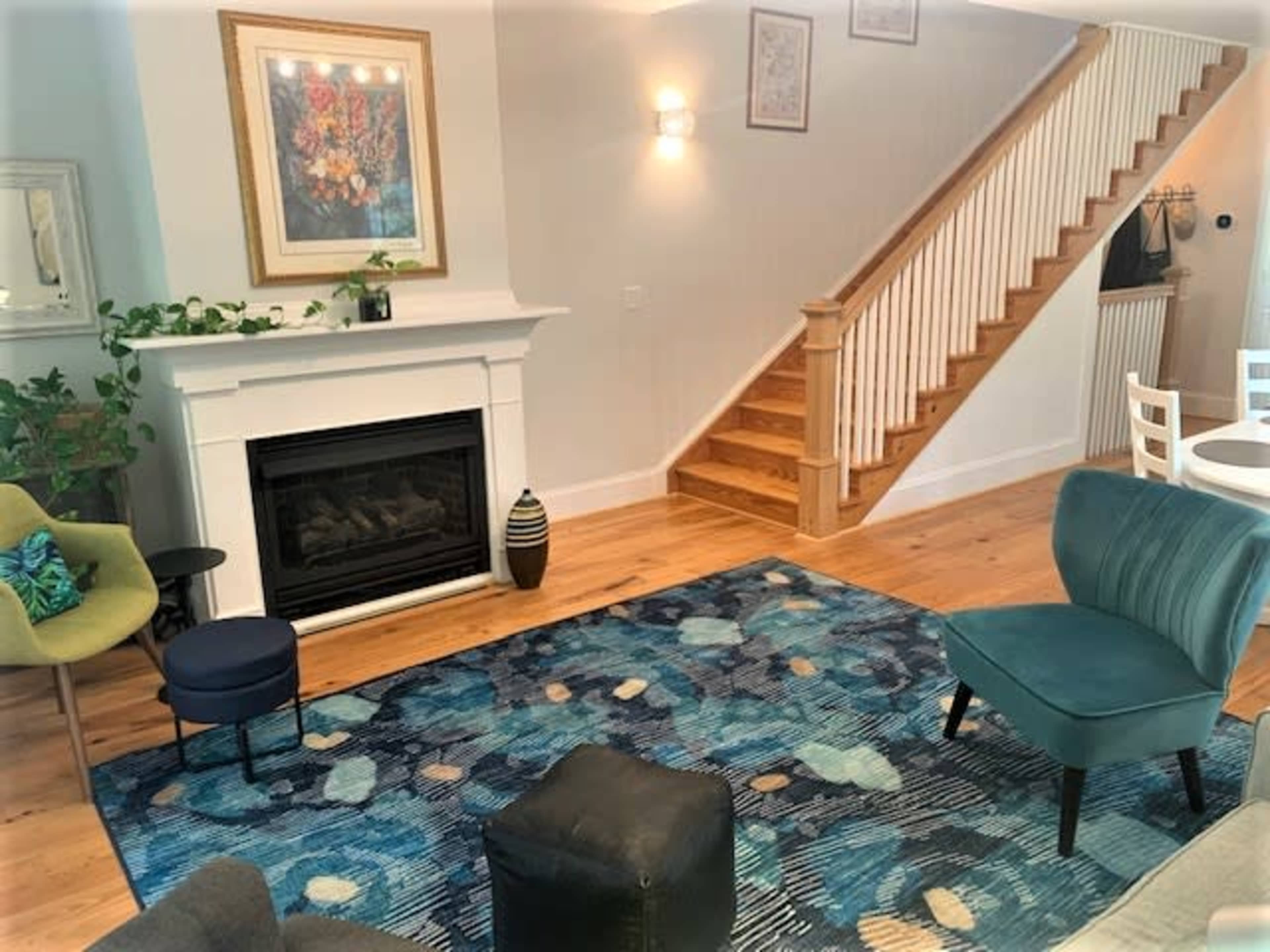 The living room features a fireplace, a variety of seating options, a decorative rug, and a staircase in the background.