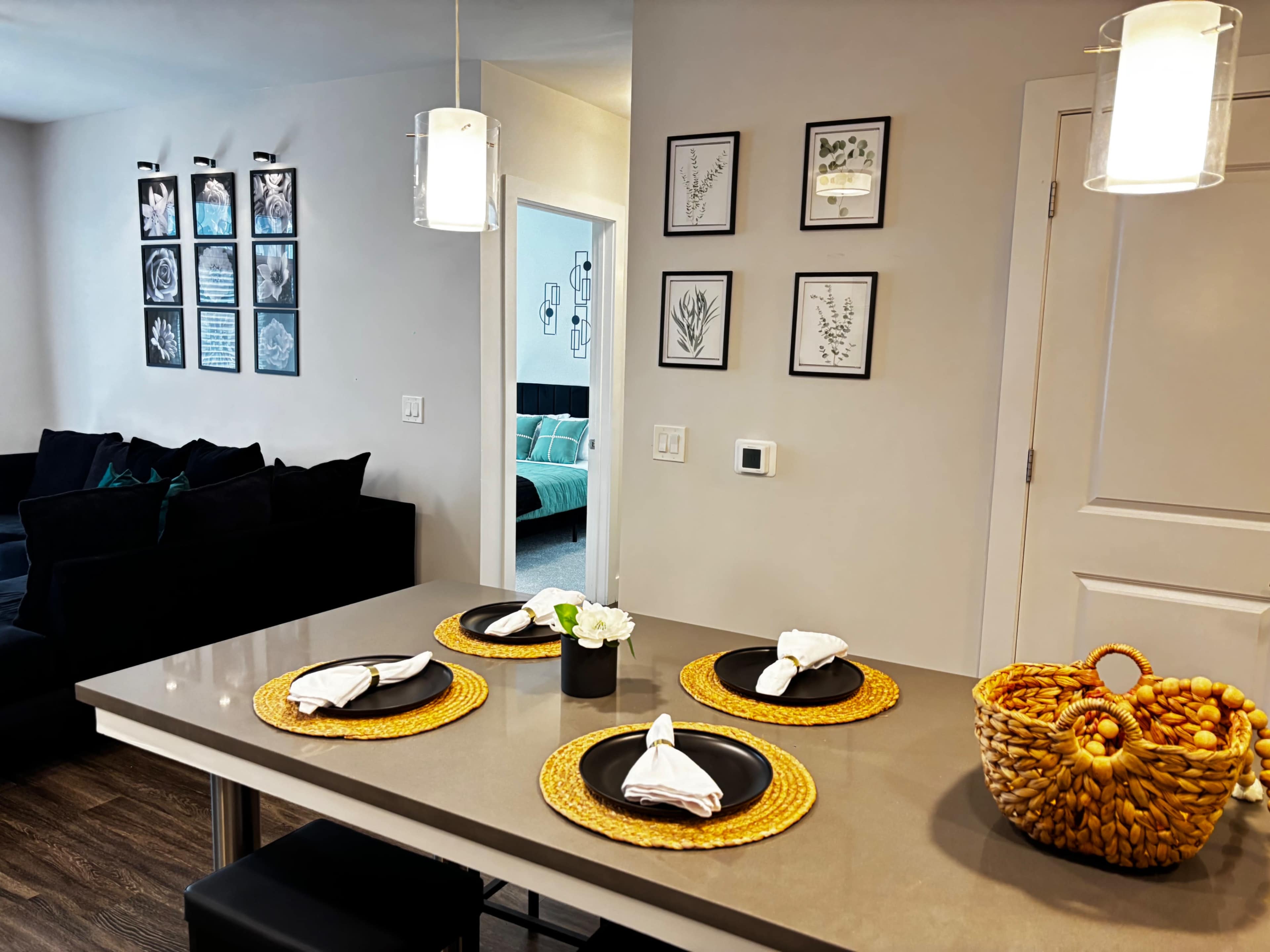 The image shows a modern dining area with a grey table set for four and surrounded by a black sofa and decorative wall art.