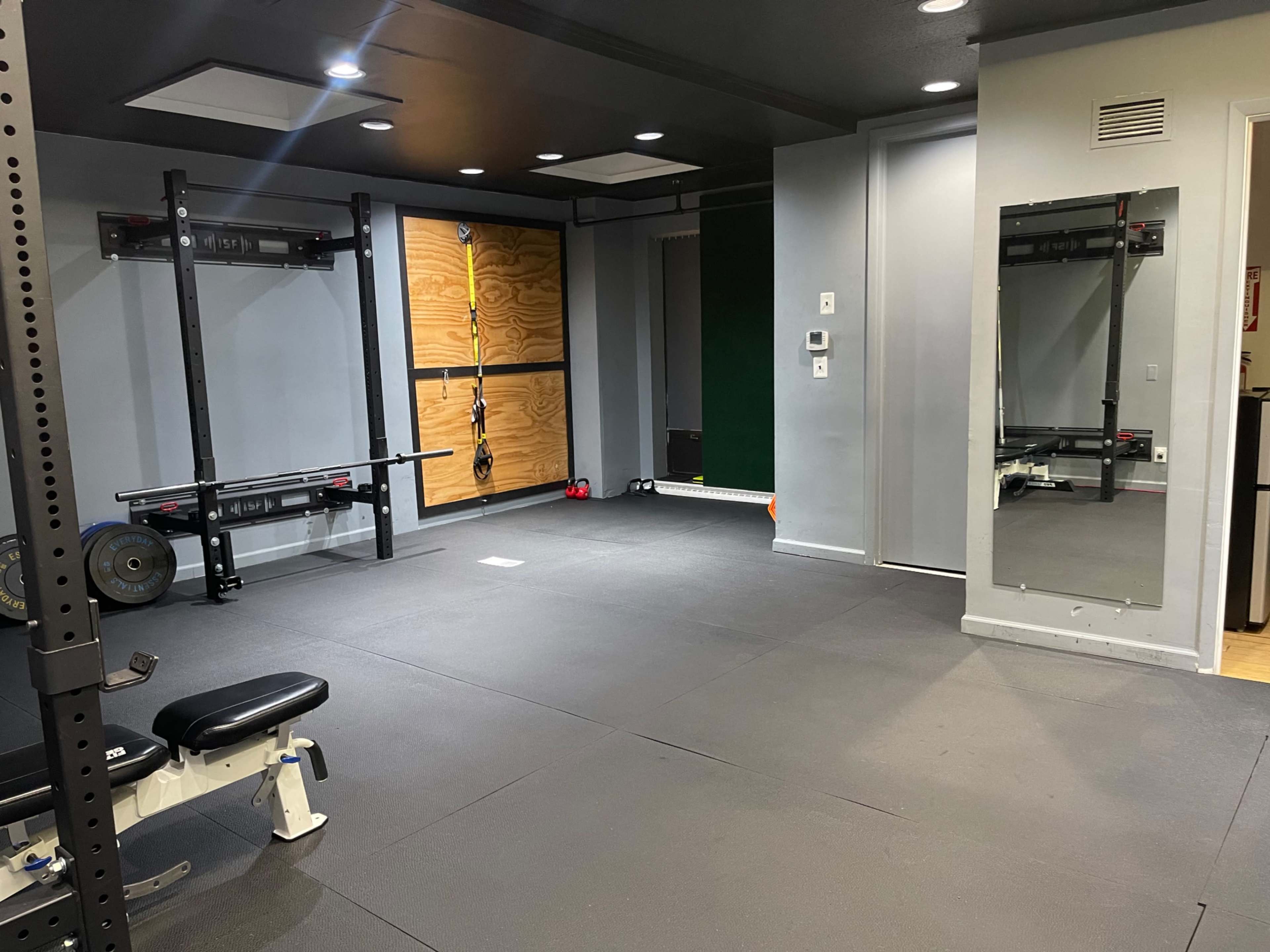 A home gym with exercise equipment, including a weight bench, barbell rack, and a large mirror on one wall.
