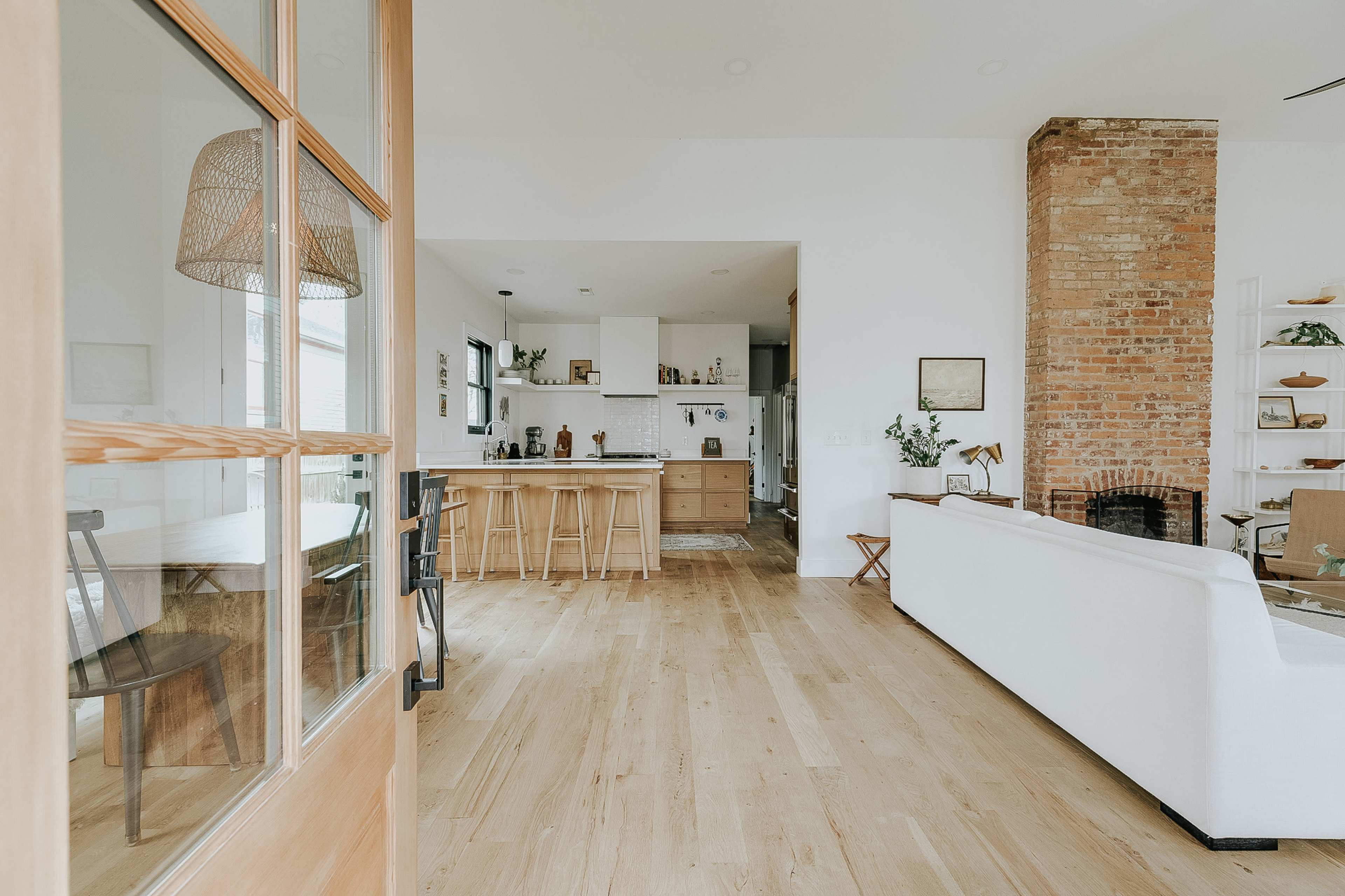A welcoming interior features a bright open space with a modern kitchen, wooden flooring, and a brick accent wall.