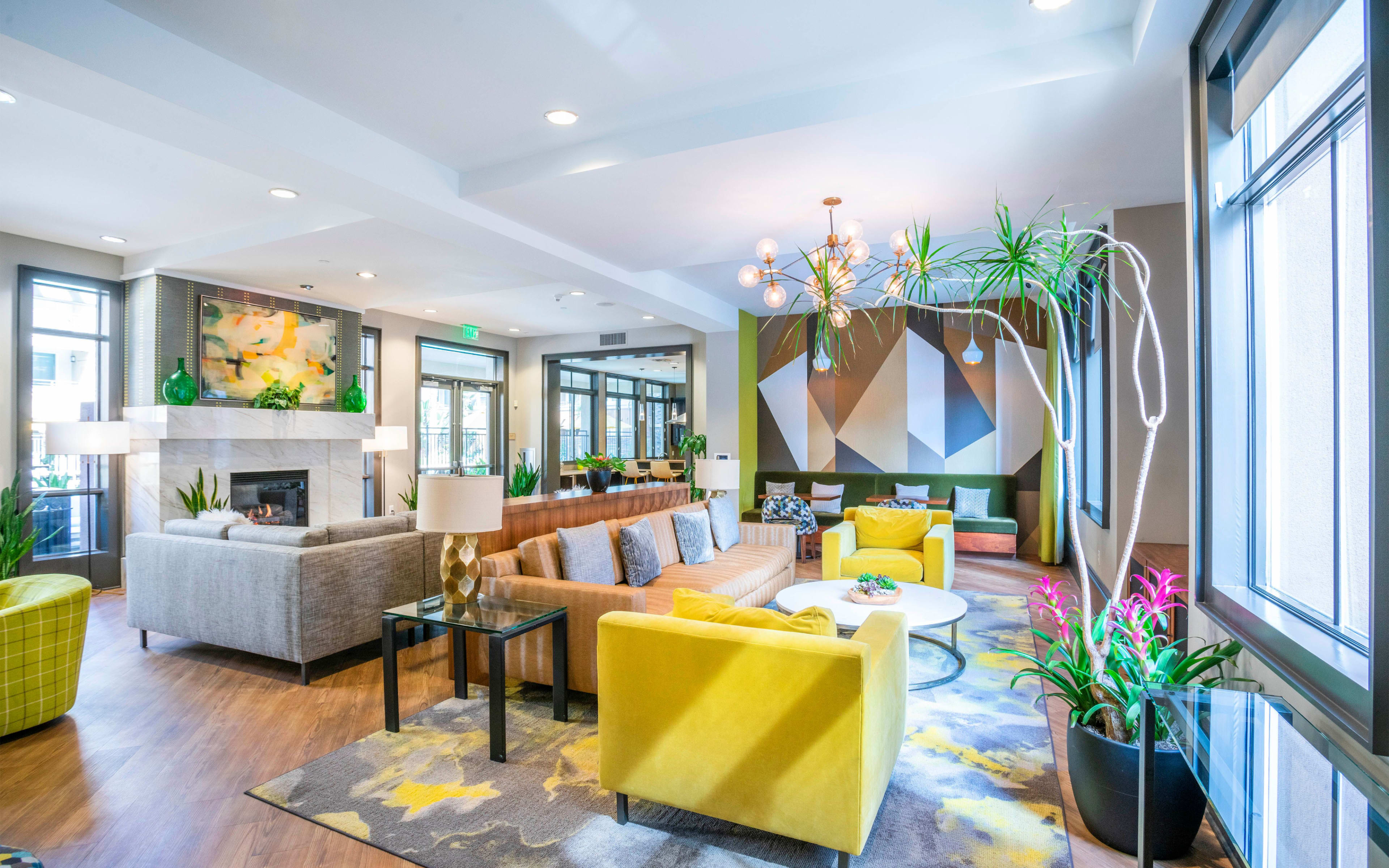 A modern lounge area featuring a combination of colorful furniture, a large sectional sofa, and decorative plants, along with a fireplace and contemporary lighting fixtures.