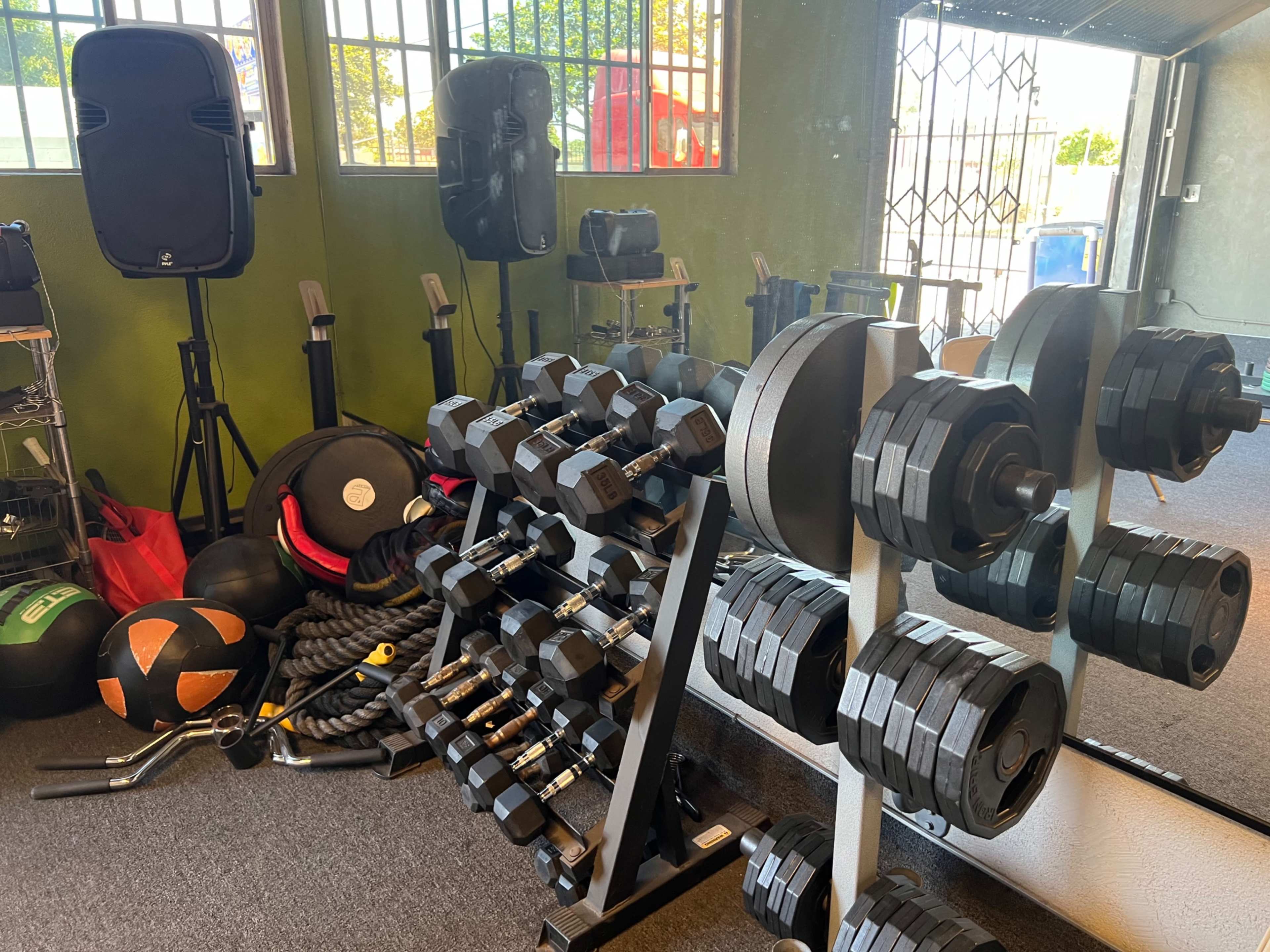 The image shows a fitness room with a rack of dumbbells, exercise equipment, and weights scattered on the floor.