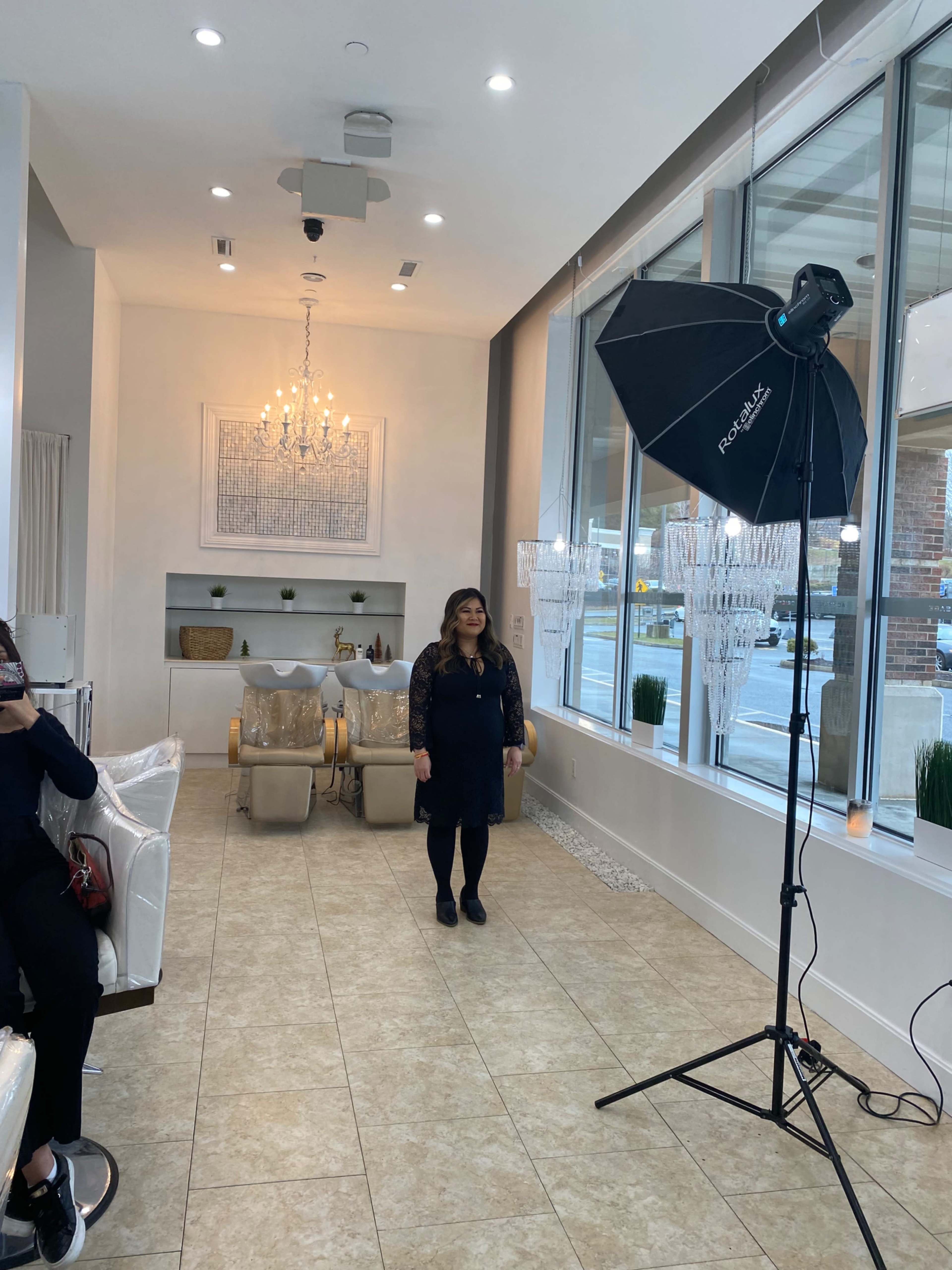 A woman stands posing in a well-lit, modern interior that features elegant decor and a large window.