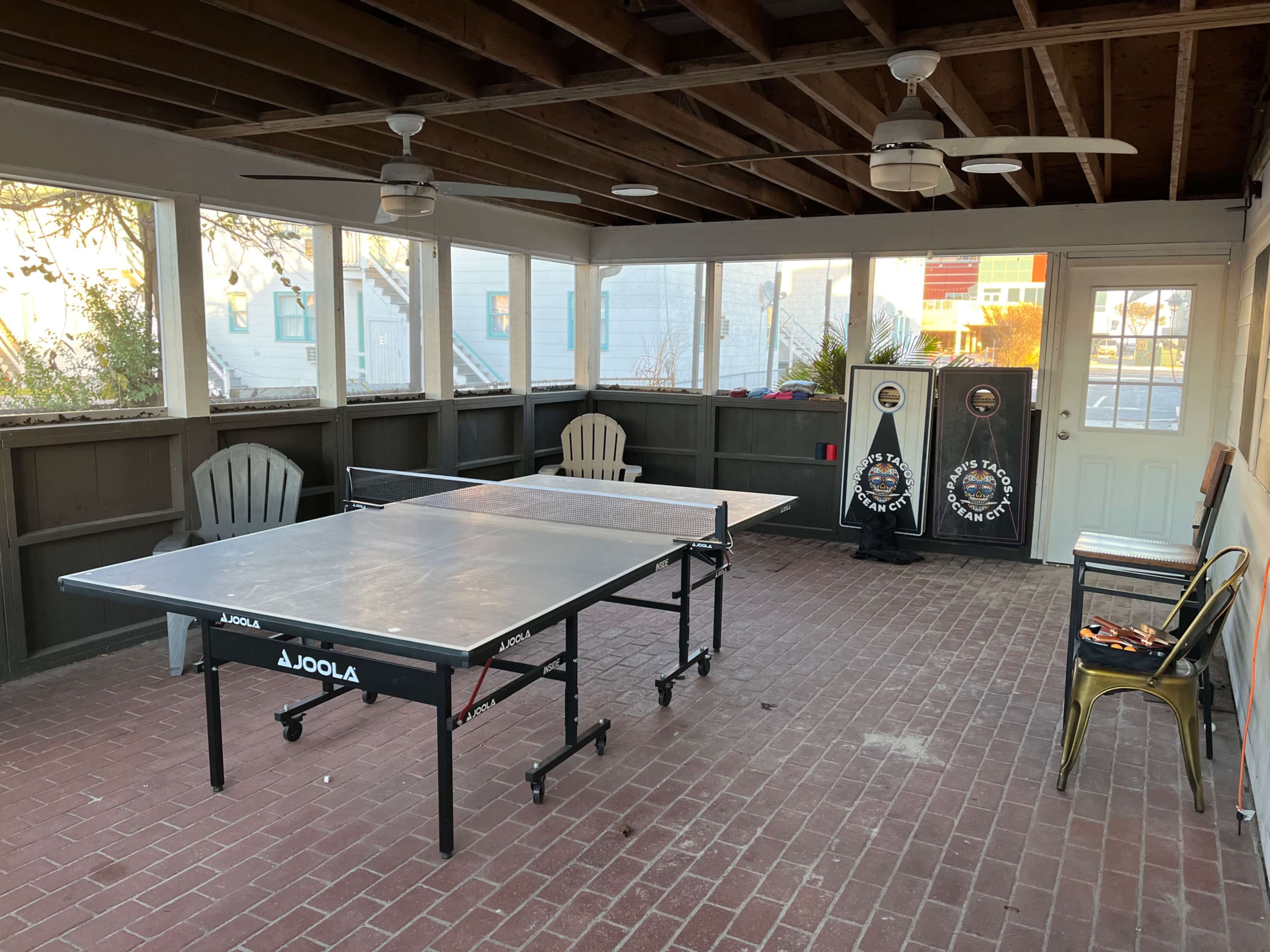 A screened porch with two table tennis tables and a dartboard setup against the wall.