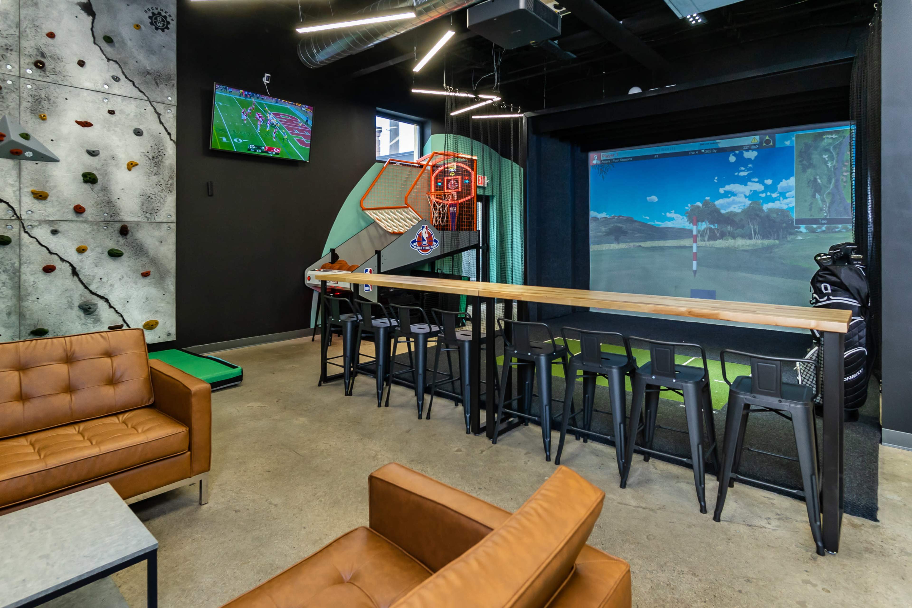 The scene features a modern recreational space with a simulated golf setup, sports screens on the walls, and seating areas including a brown leather couch and a long bar with stools.