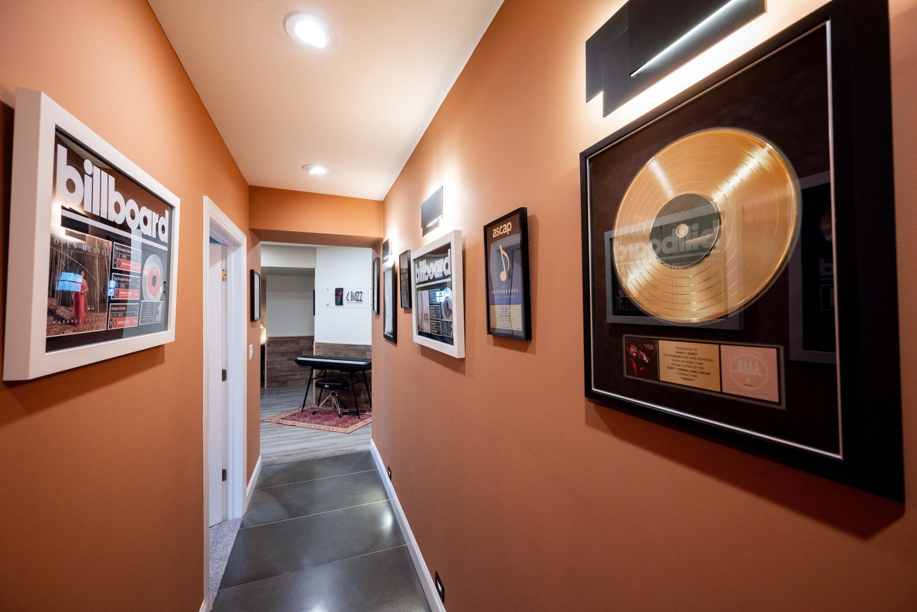 A hallway features framed music awards and gold records on the walls, leading to a piano room at the end.