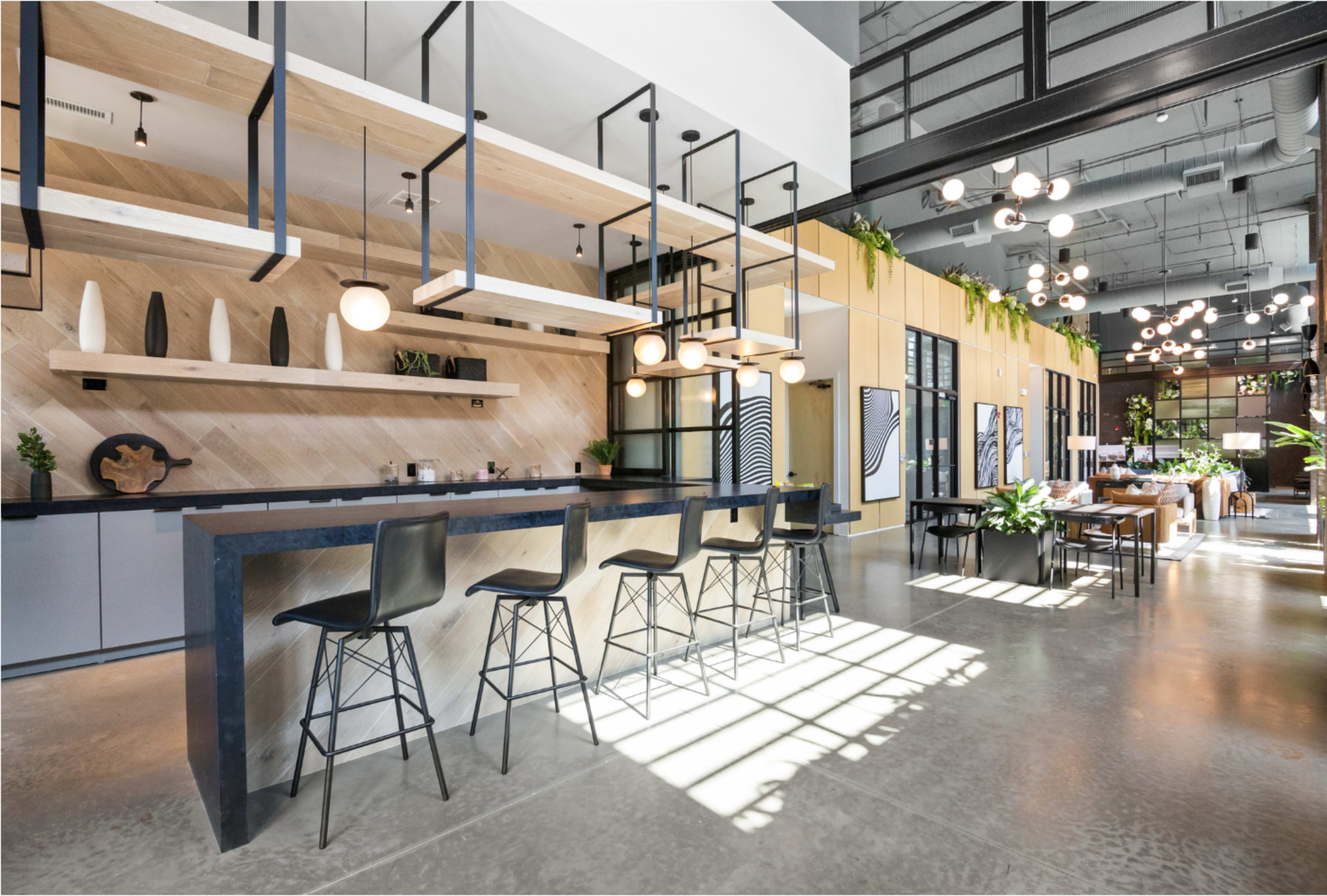 The image shows a modern, open-concept lobby with a bar area featuring high stools, sleek shelving, and plants integrated into the decor.