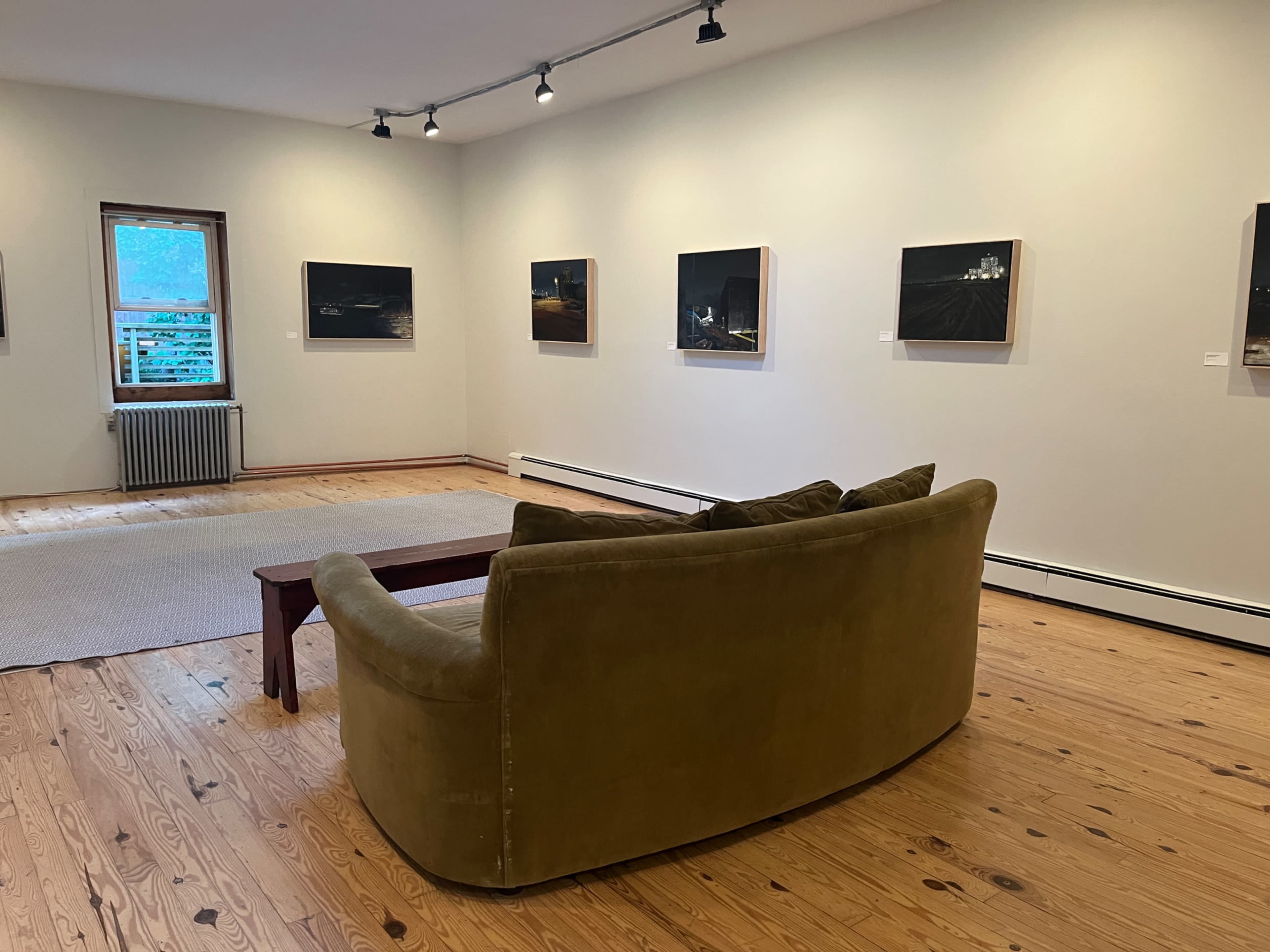 The image shows a cozy seating area with a green couch and a wooden coffee table, set against a gallery wall displaying several framed photographs.
