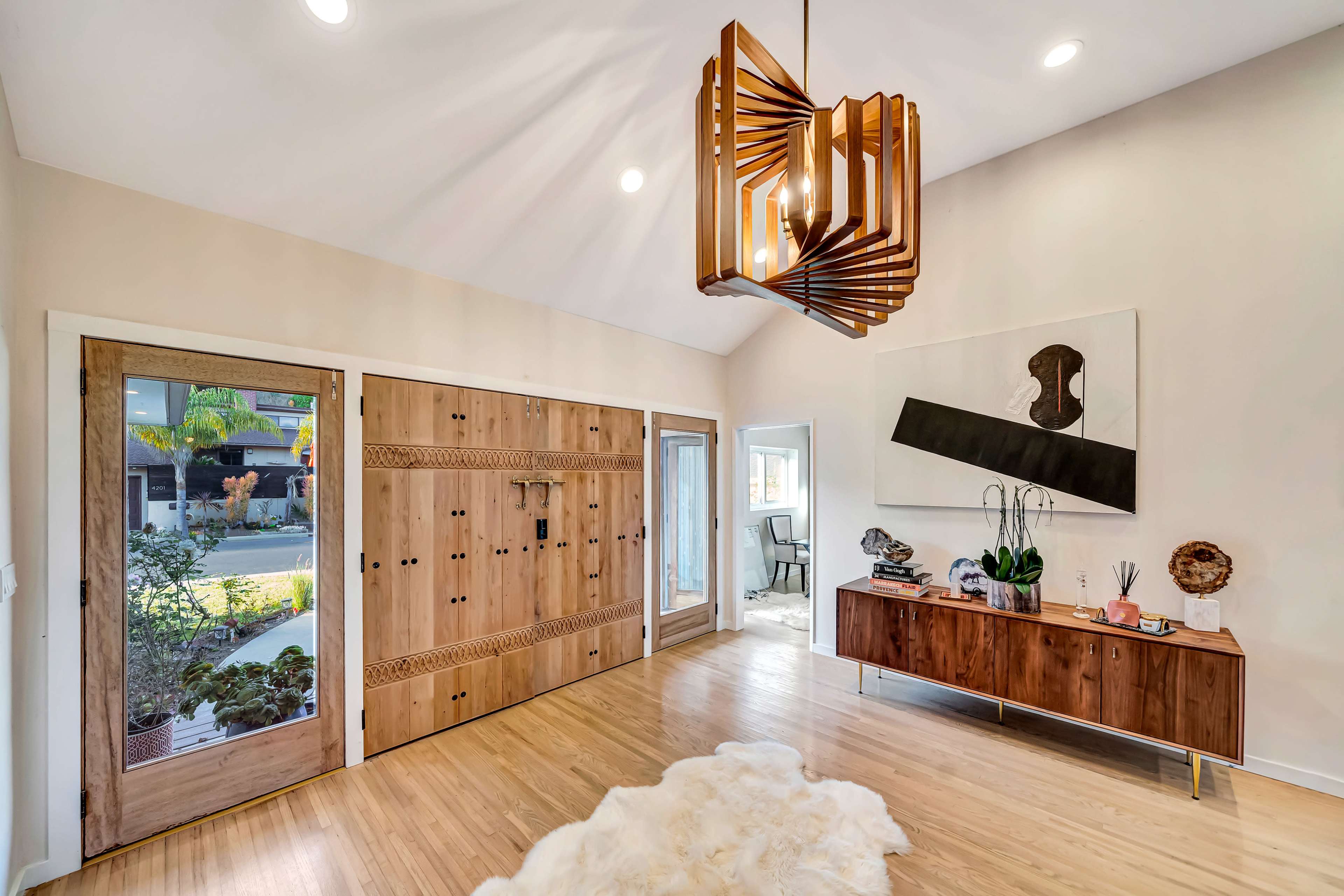 A spacious entryway featuring a wooden front door, a contemporary chandelier, and a sideboard with decorative items.