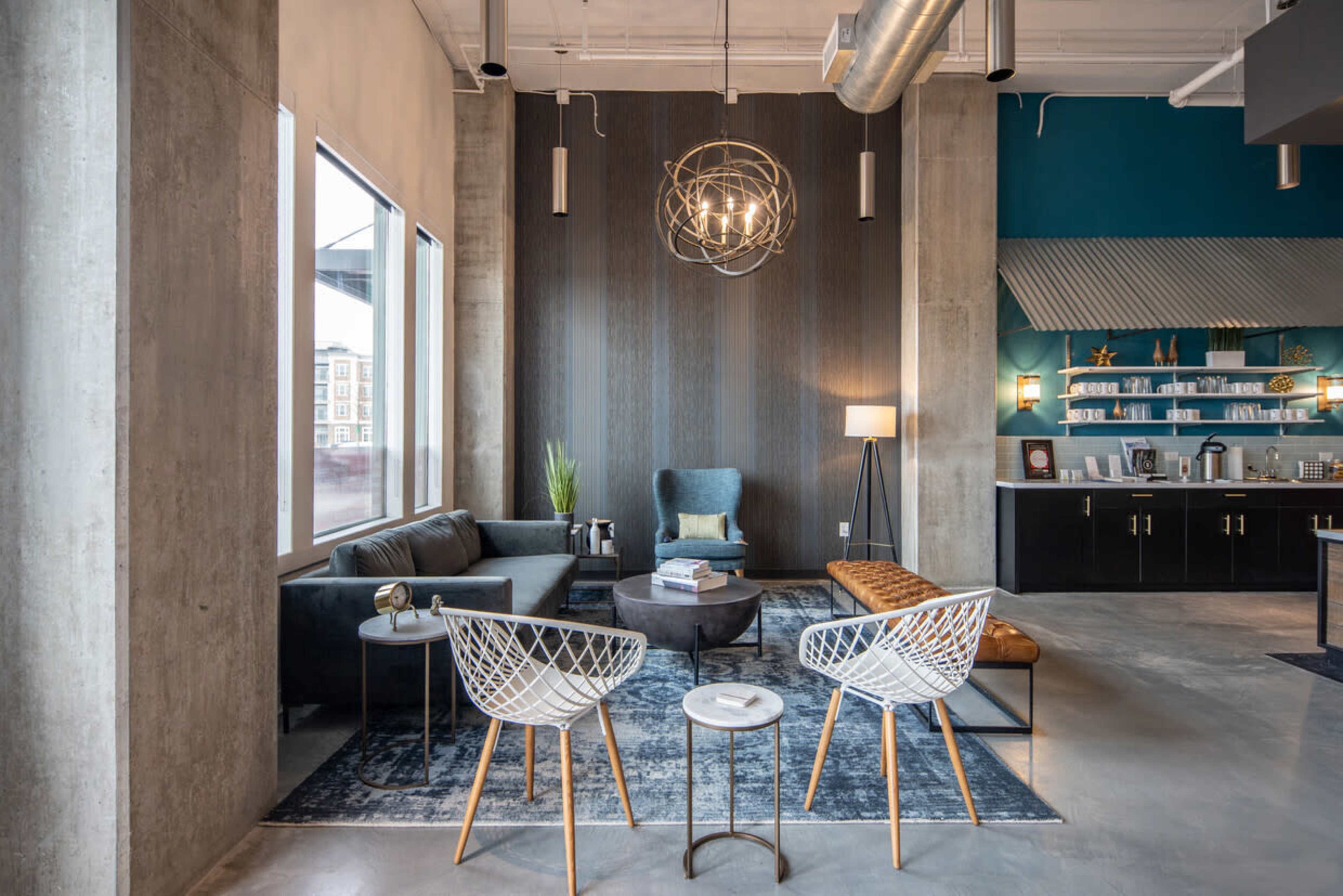 A modern lounge area featuring a dark sofa, a set of white chairs, a round coffee table, and a decorative wall with an overhead light fixture.
