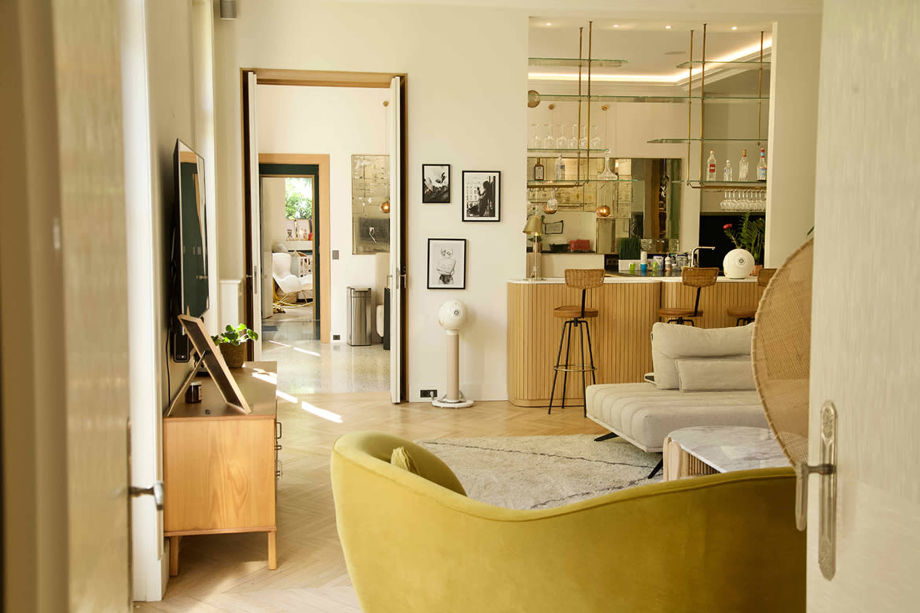 A modern interior showcases a living area with a yellow chair, a gray sofa, and a view into a kitchen with a bar.