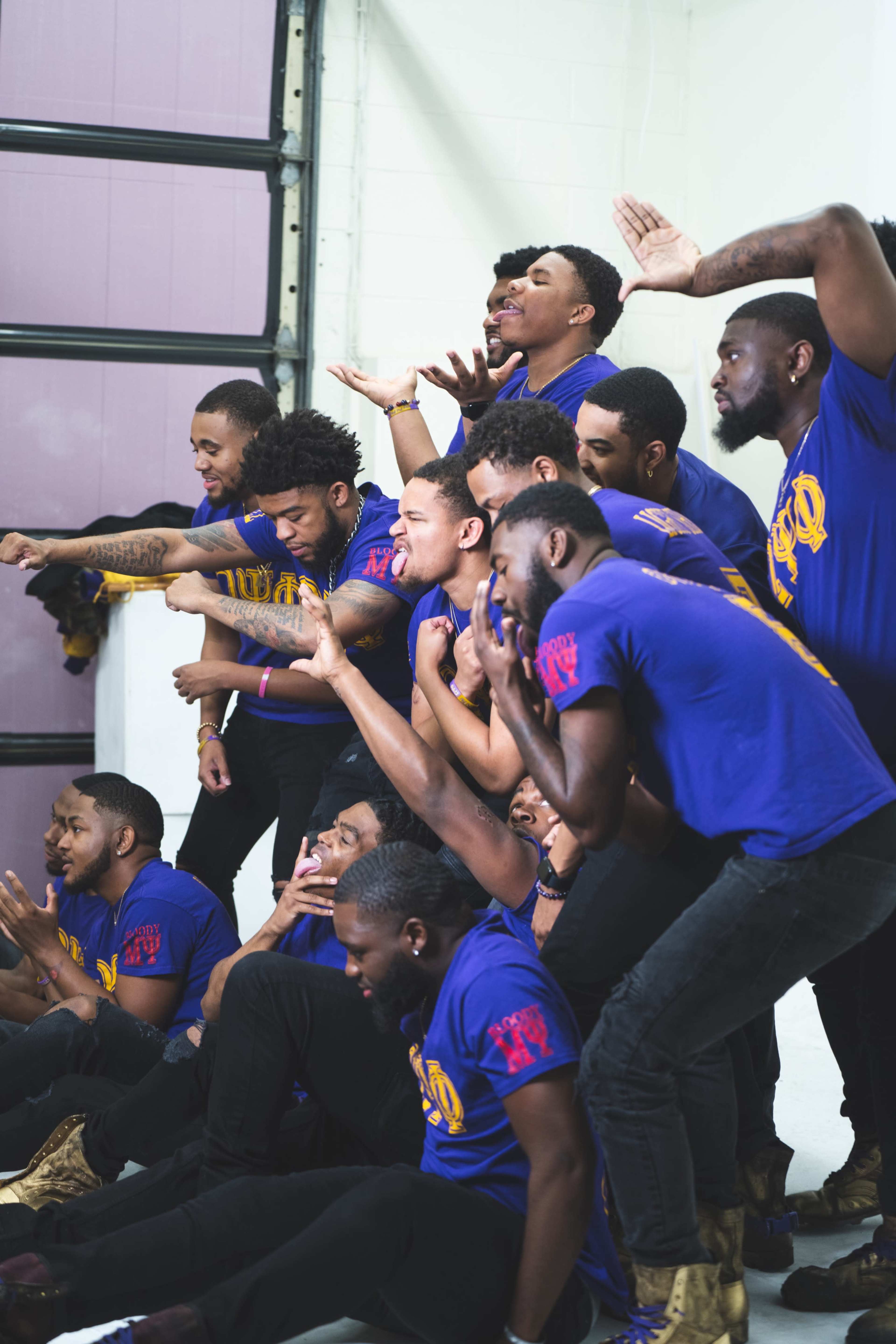 A group of young men in blue shirts poses together, displaying various expressions and gestures in a dynamic arrangement.