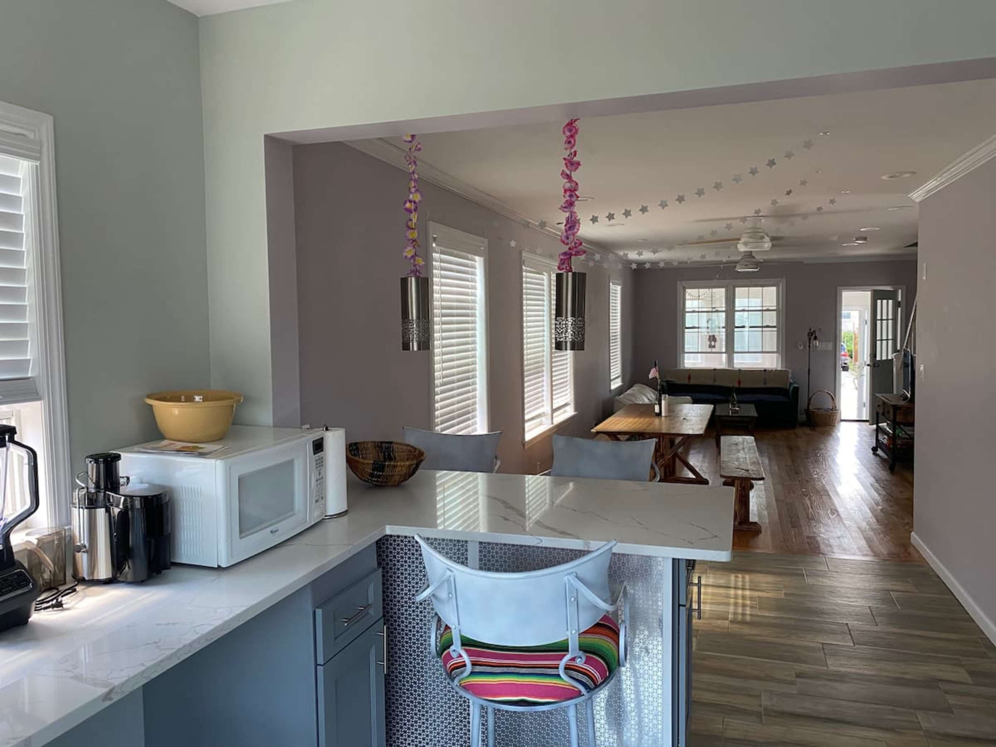 A modern kitchen area with a microwave, a bowl of fruit, and a barstool, leading into a living room with a table and couch.