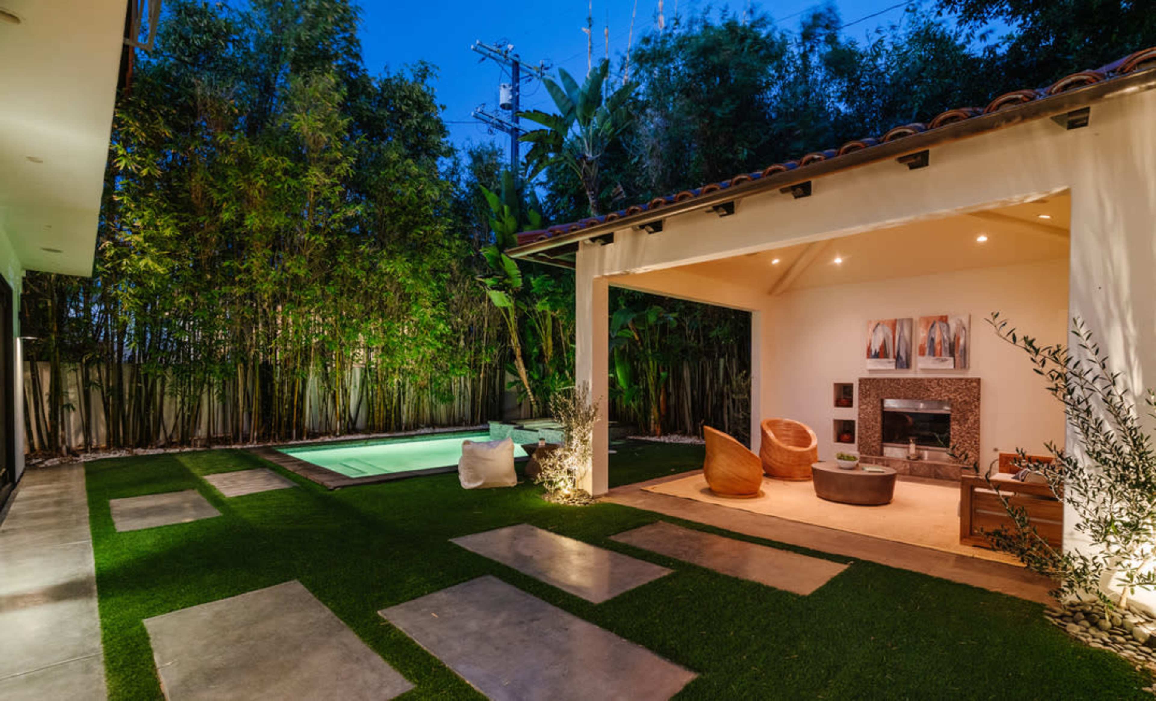 A modern outdoor space featuring a small swimming pool, manicured grass, a seating area with stylish furniture, and surrounding greenery.