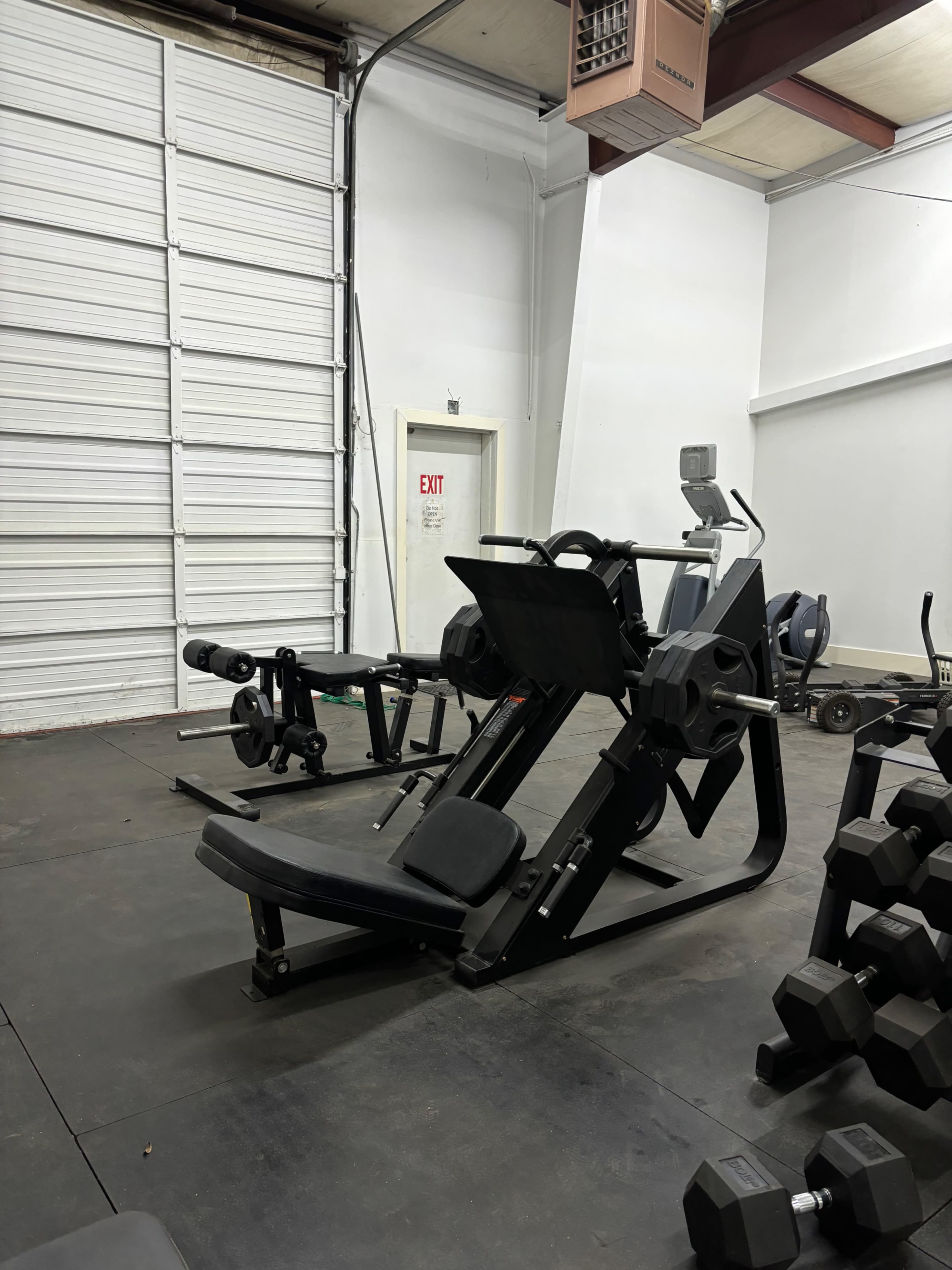 A gym interior featuring a leg press machine, an exercise bike, and various weightlifting equipment.