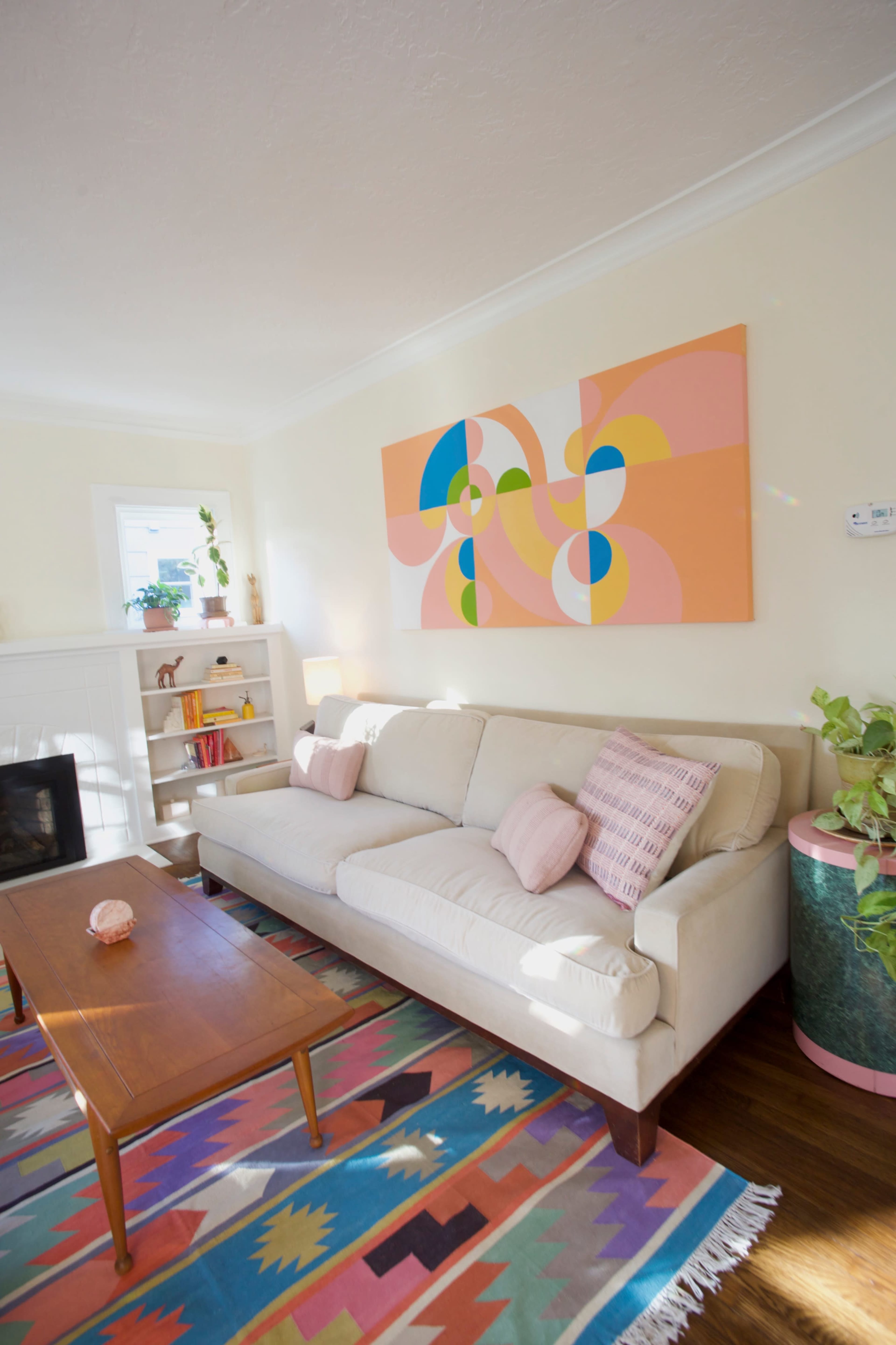 A bright living room with a light-colored sofa, a wooden coffee table, and a colorful area rug, featuring a large abstract artwork on the wall.