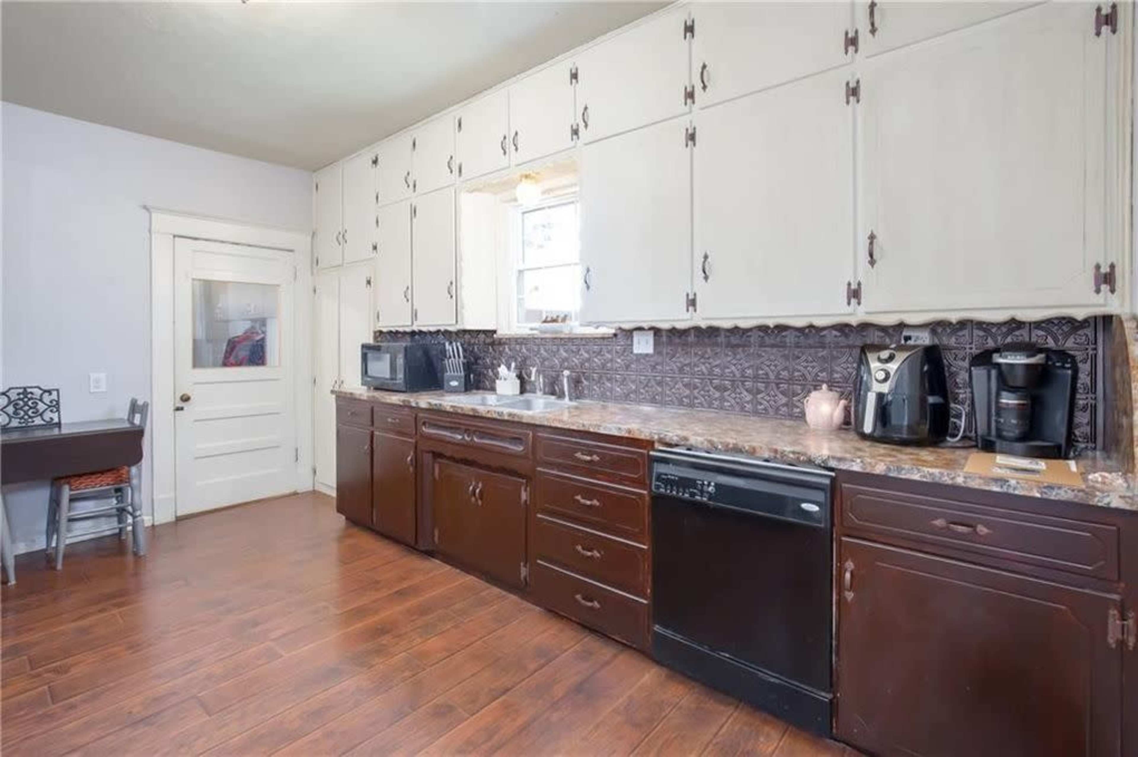 The image shows a kitchen with dark wooden cabinets, a granite countertop, and various appliances including a coffee maker and a microwave.