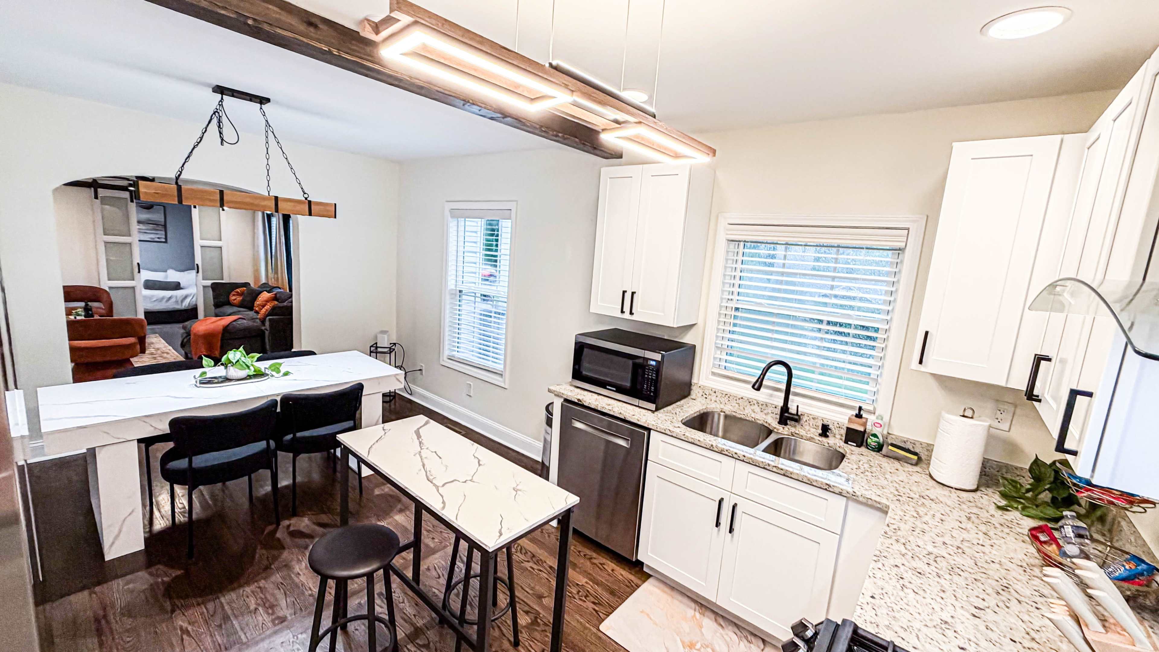 The image shows a modern kitchen with white cabinets, a granite countertop, and a small dining area with black chairs and a table.