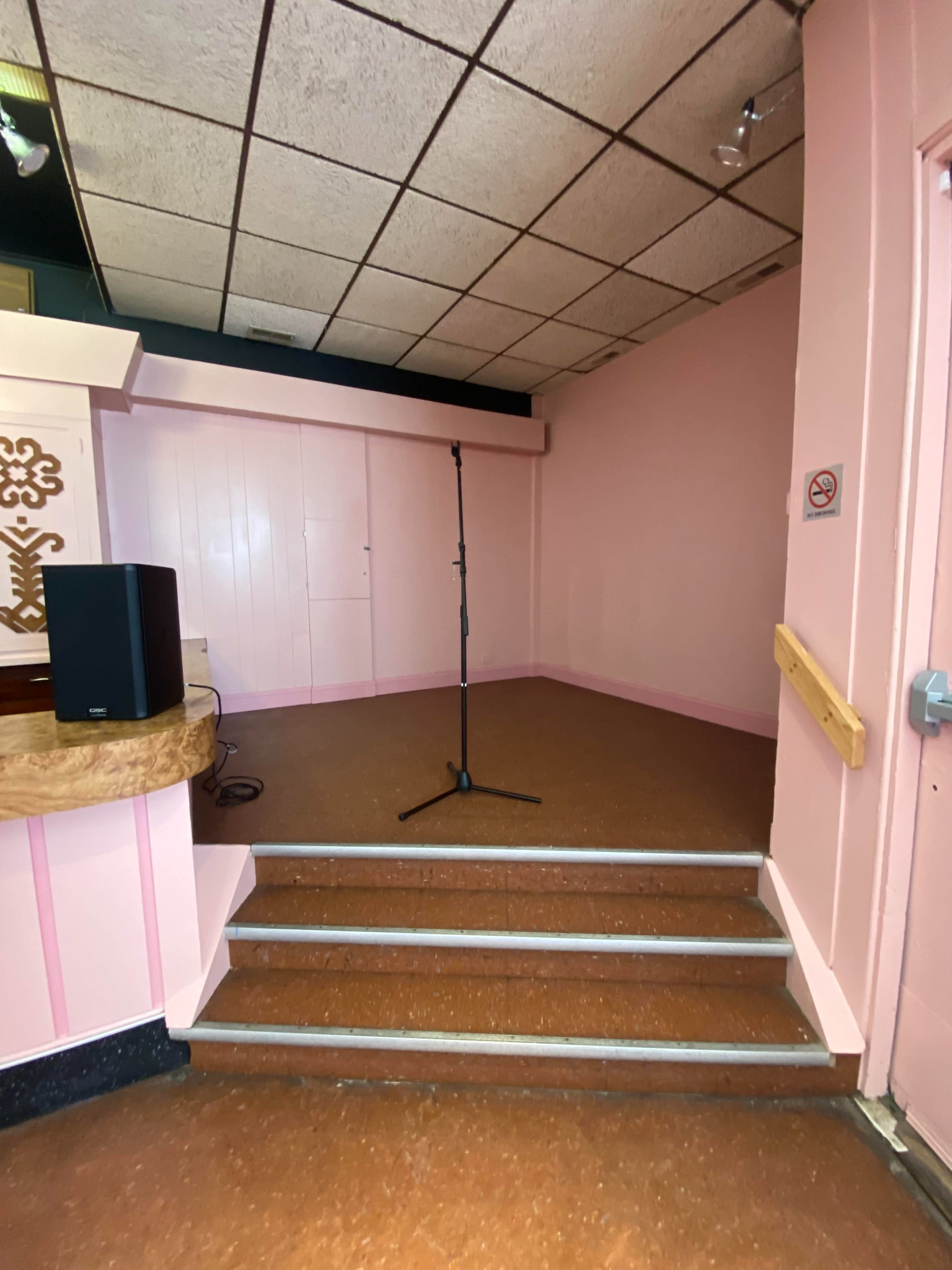 A small stage area with a microphone stand, surrounded by pink walls and a few steps leading up to it.