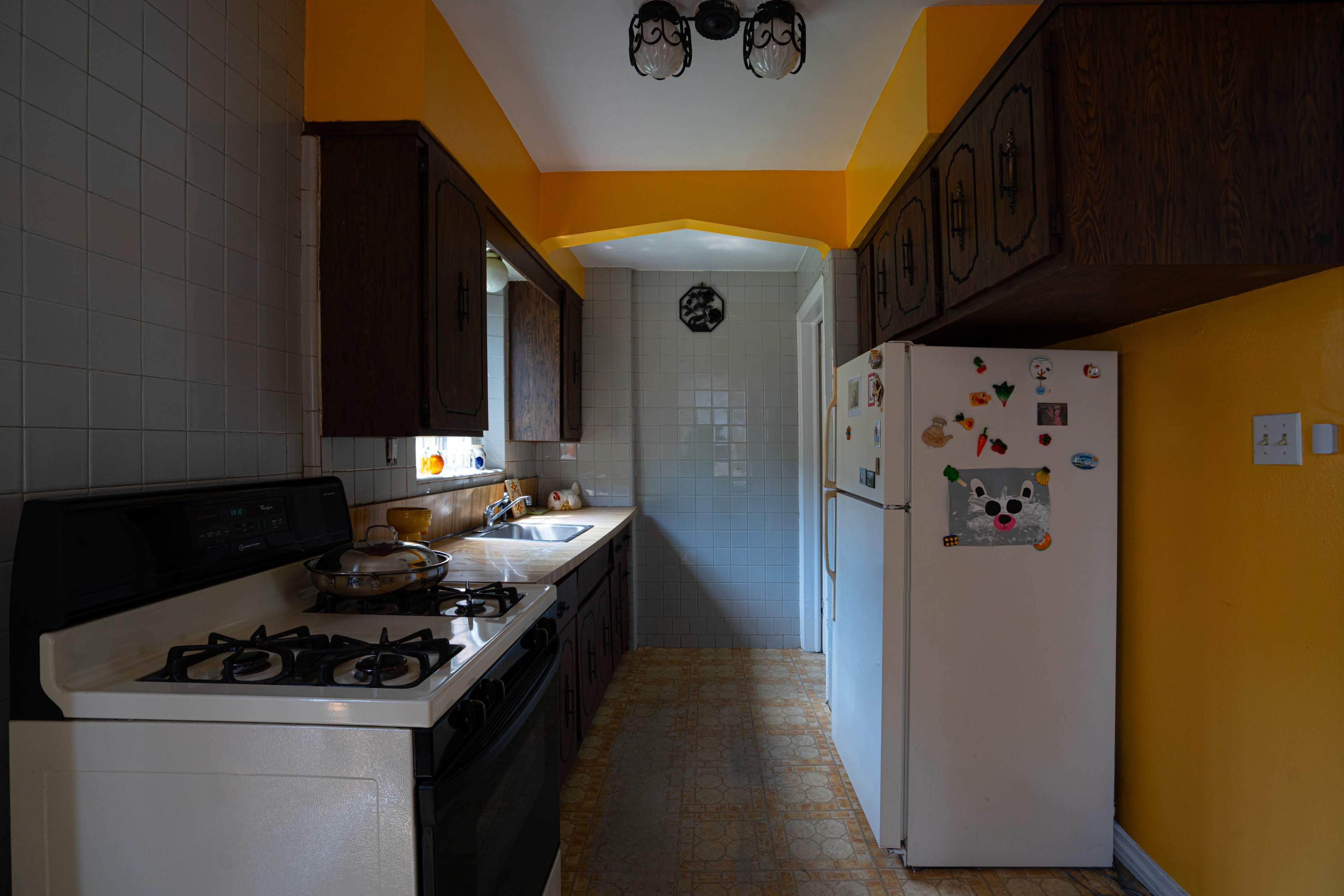 The kitchen features dark wooden cabinets, a white stove, and a refrigerator adorned with magnets, all set against orange and blue walls.