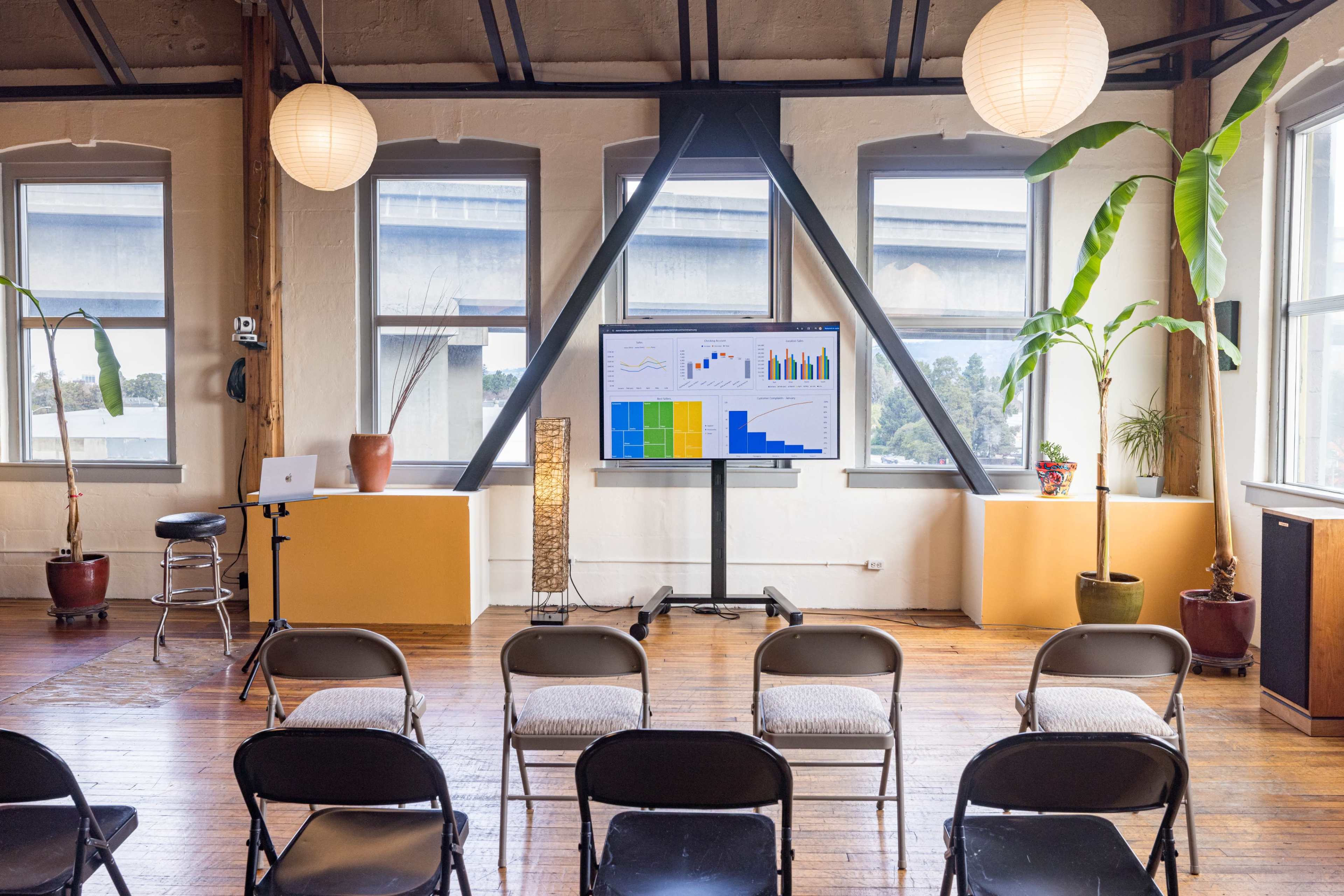 A modern seminar room features empty chairs facing a large screen displaying colorful graphs, with potted plants and soft lighting.