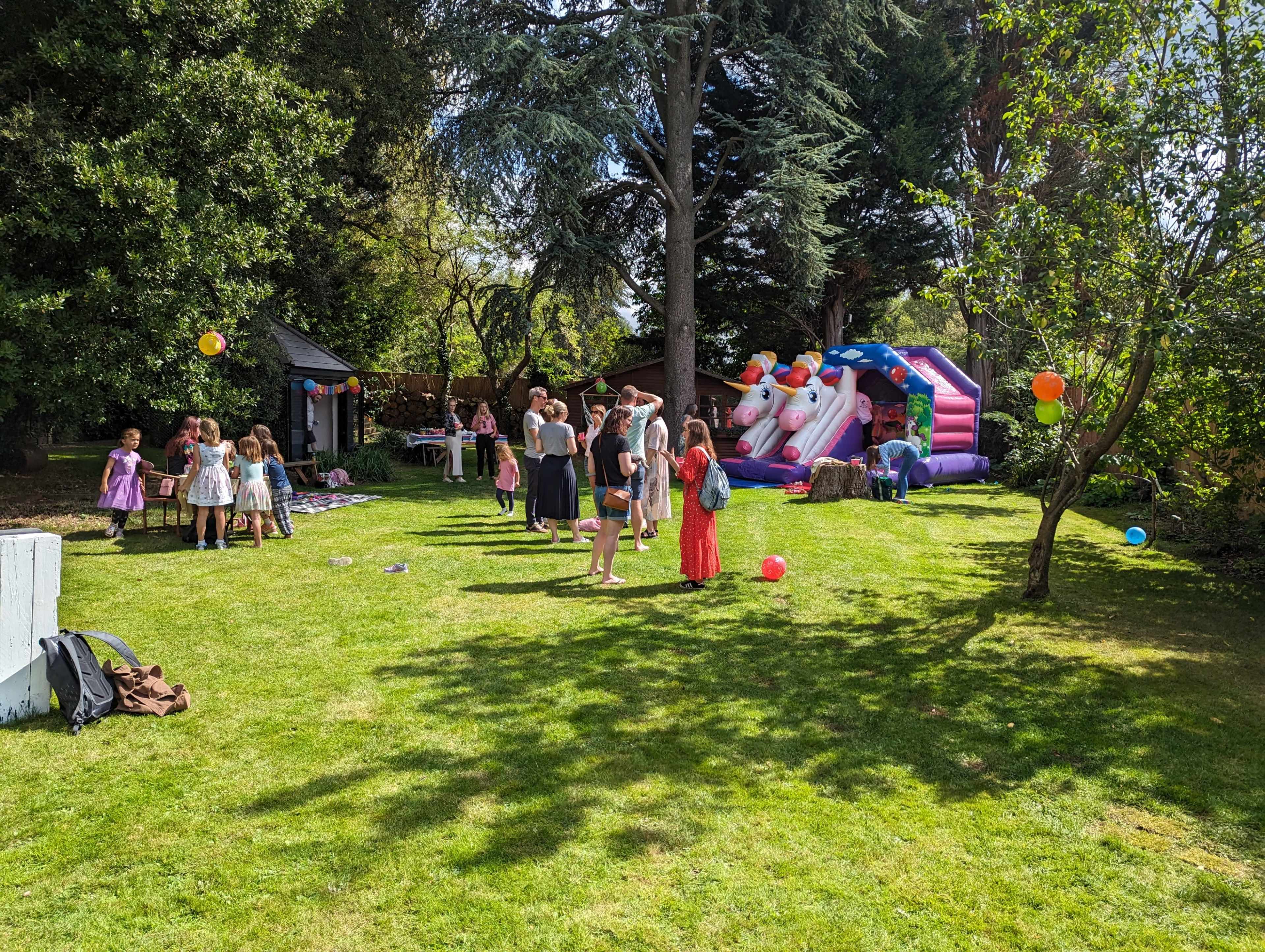 A group of children and adults gather in a backyard with a bounce house and various colorful decorations.