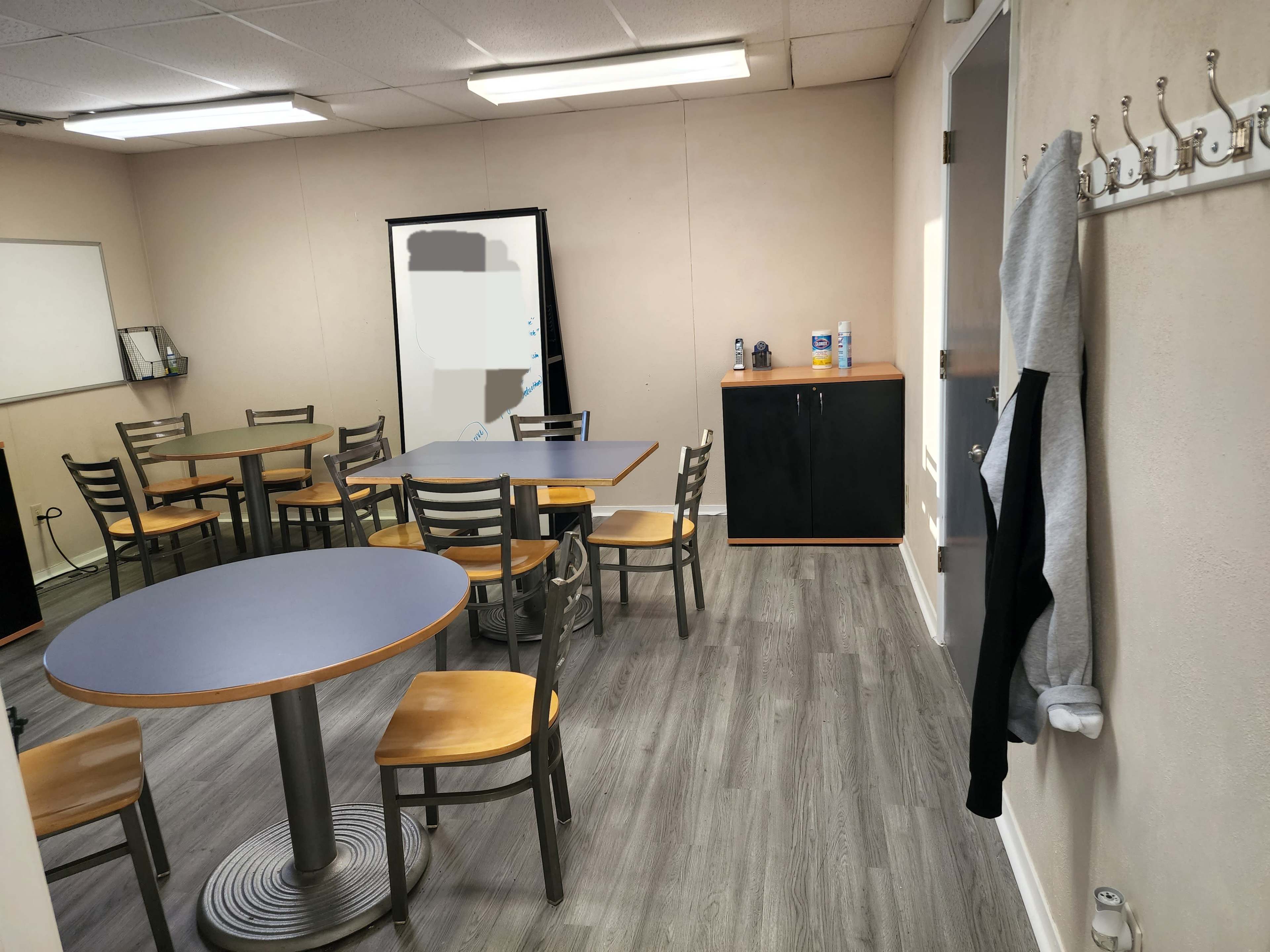 A small meeting room with several round tables, chairs, and a cabinet against the wall.