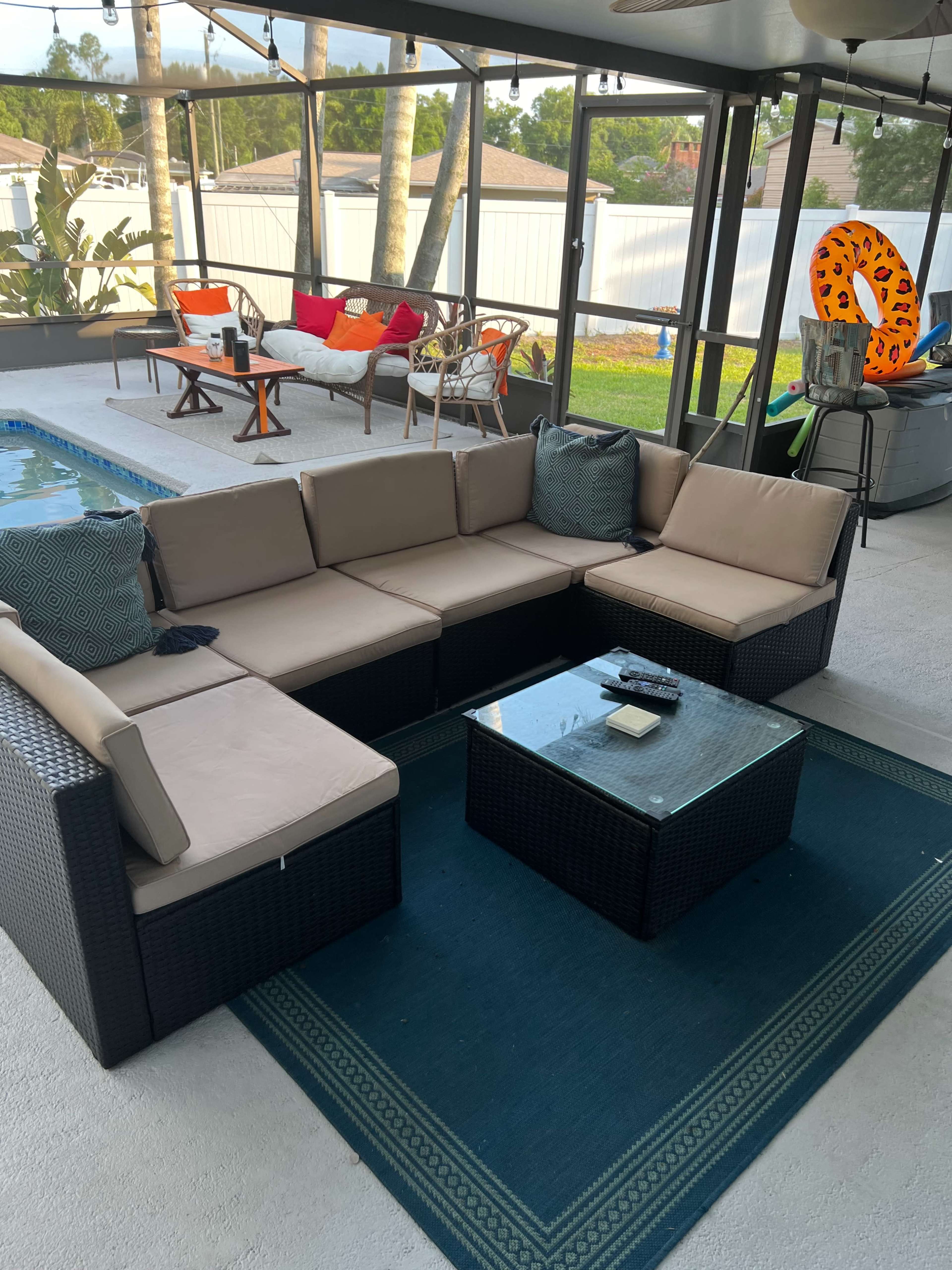 A spacious patio area with a sectional sofa, a glass coffee table, and a view of a swimming pool in a well-lit environment.